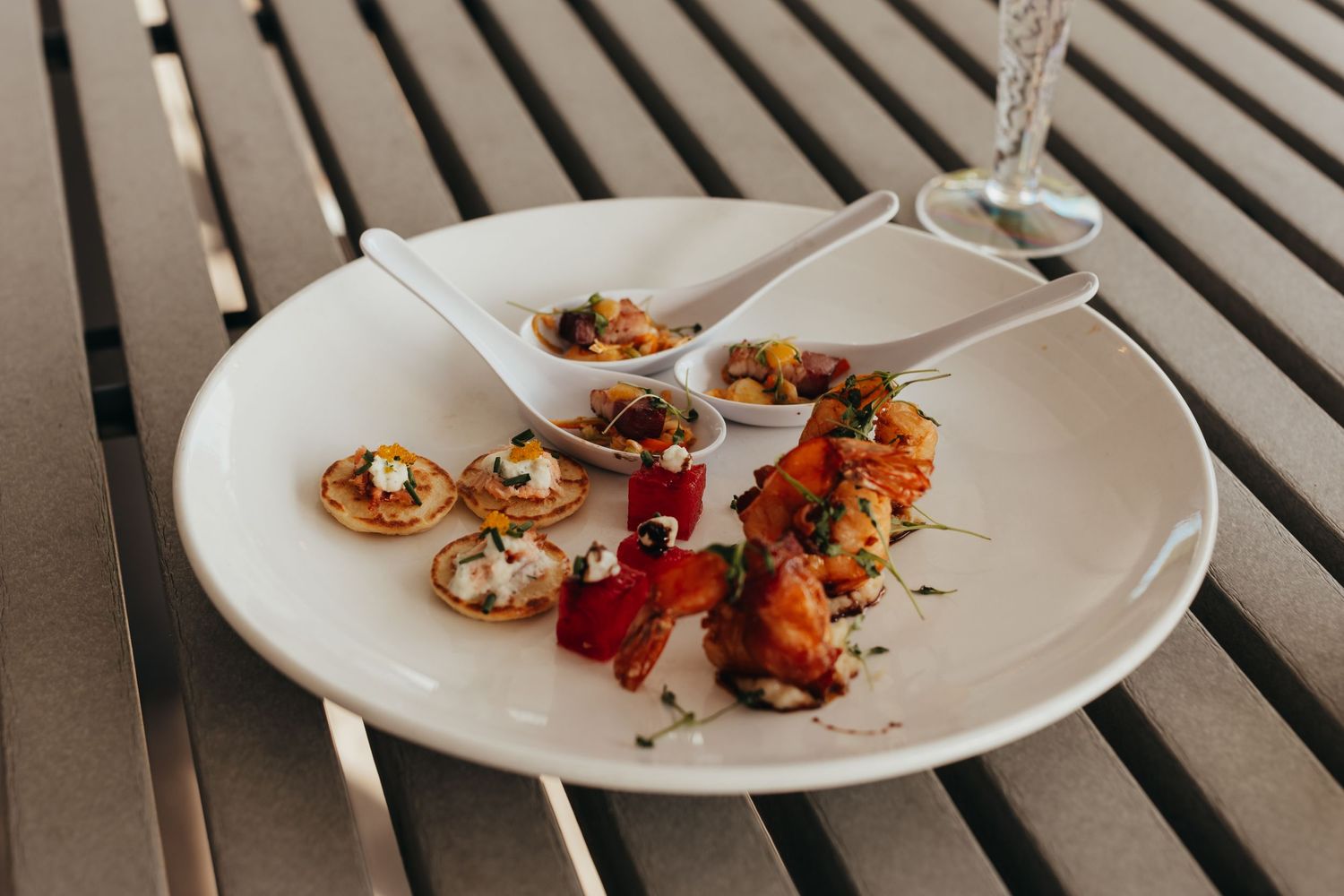 An elegant white plate with gourmet appetizers and garnishes served on a wooden surface.