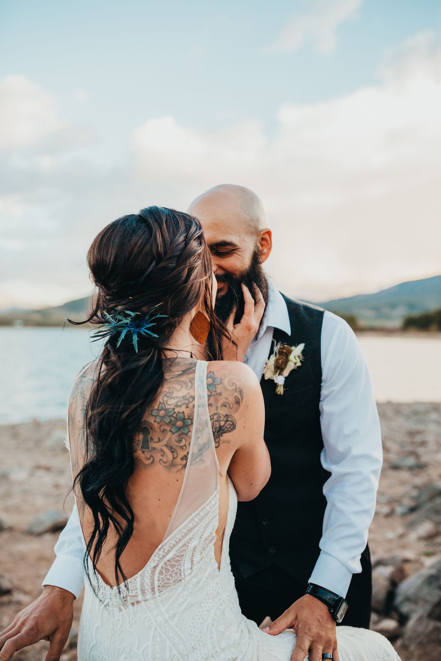 Wedding couple shares intimate moment by lake with mountains in background.
