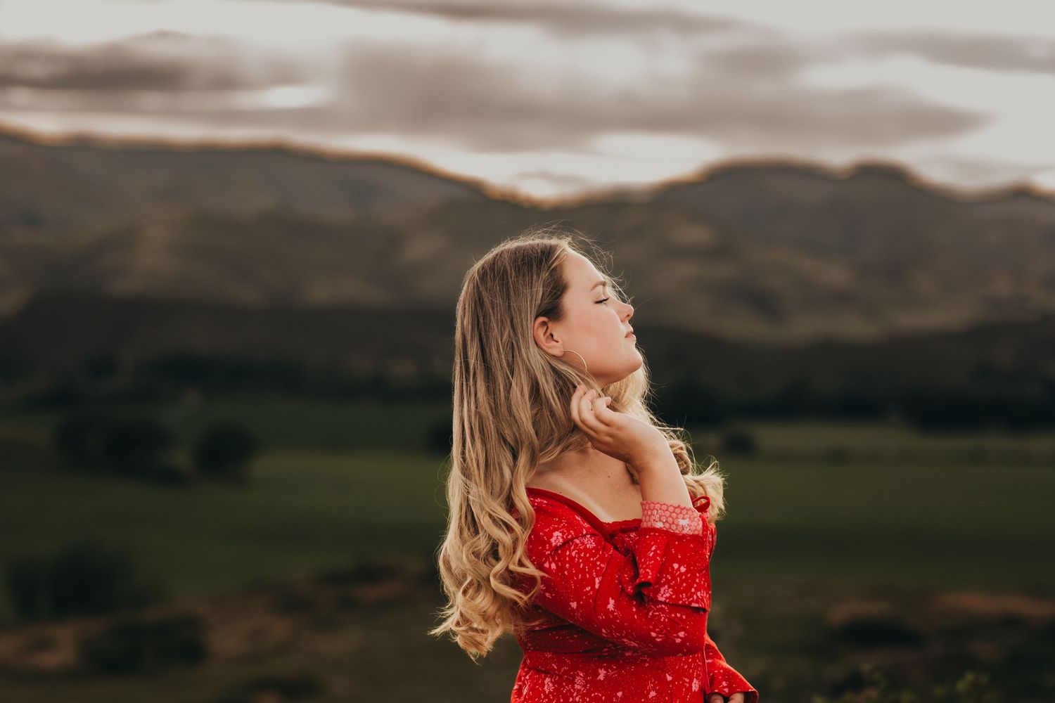 Romantic portrait of someone in red dress against mountain landscape at sunset.