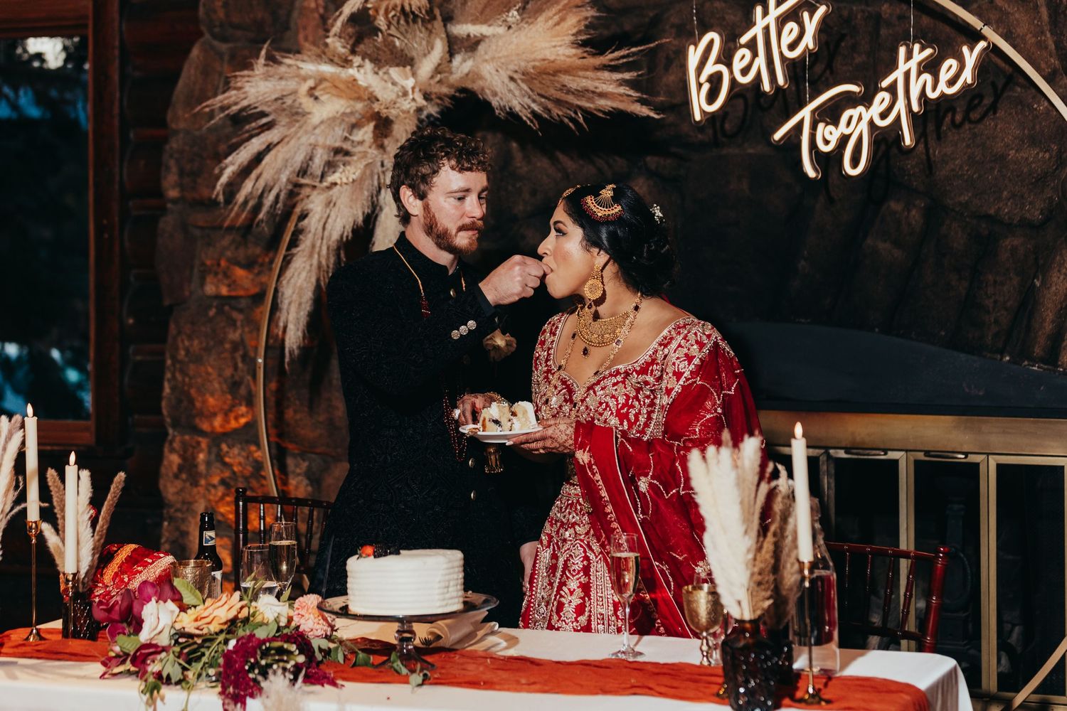 A couple sharing a moment at their wedding cake table decorated with pampas grass and a 'Better Together' sign.
