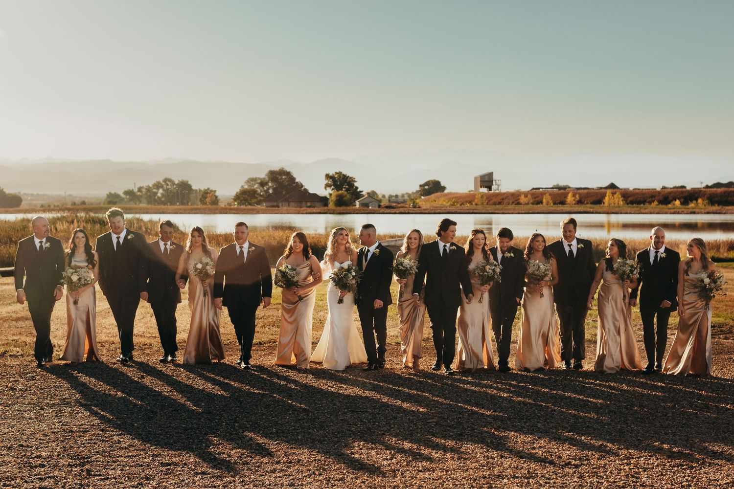 Wedding party poses at sunset on beach with golden light creating dramatic silhouettes.