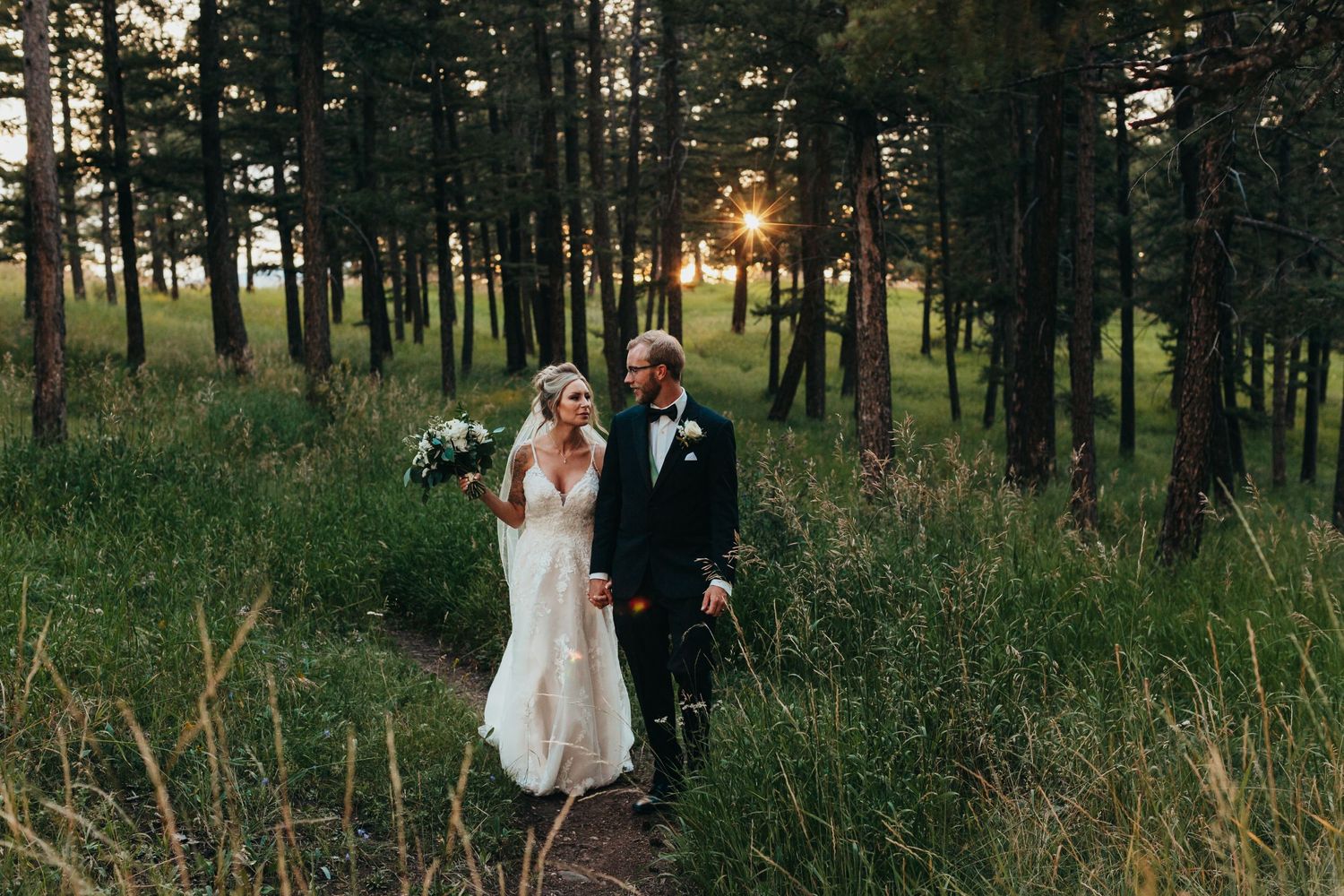A couple walks along a forest path at sunset during their wedding photoshoot.