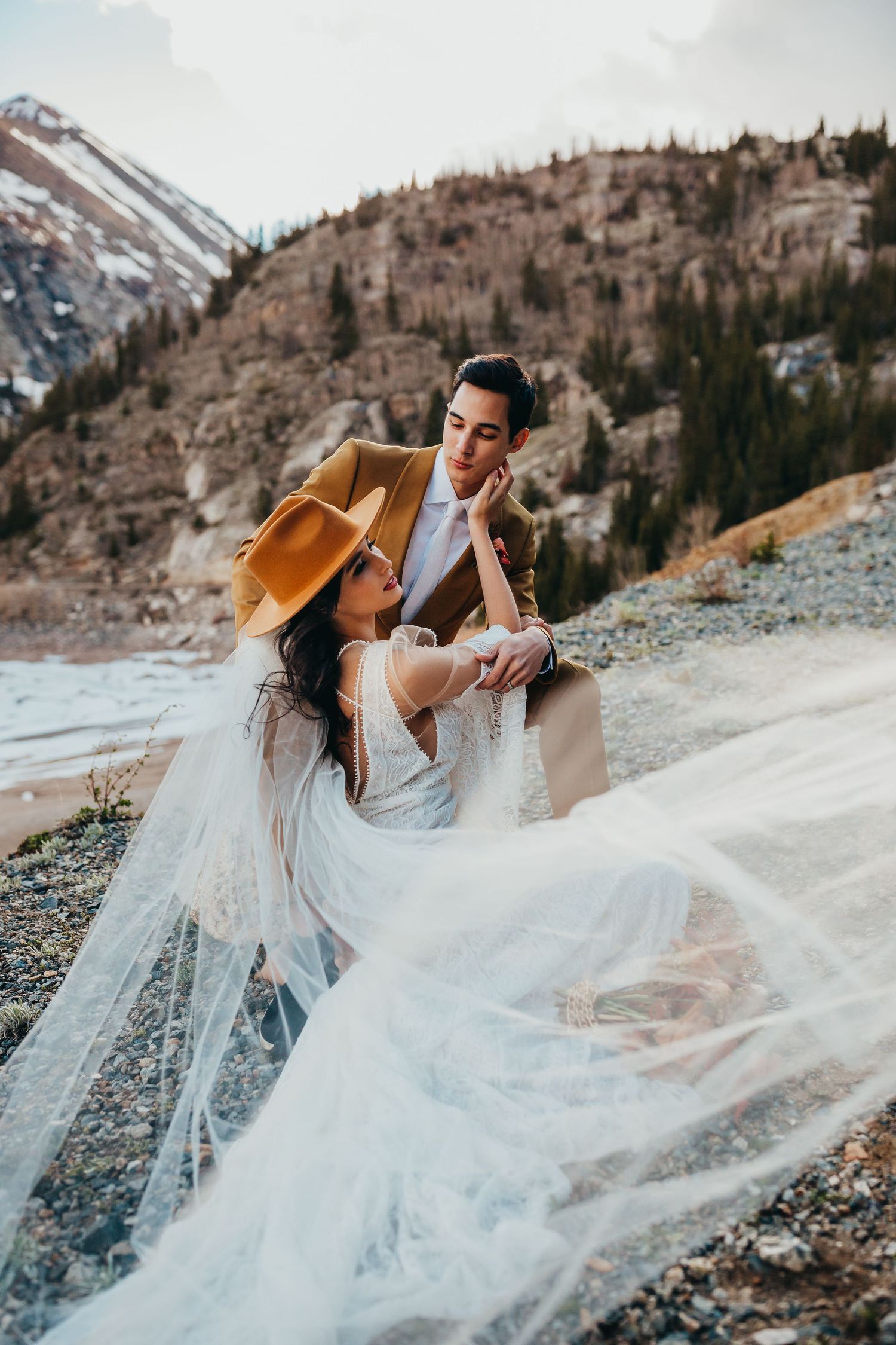 A romantic wedding photoshoot on a rocky mountainside with a flowing white veil catching the wind.