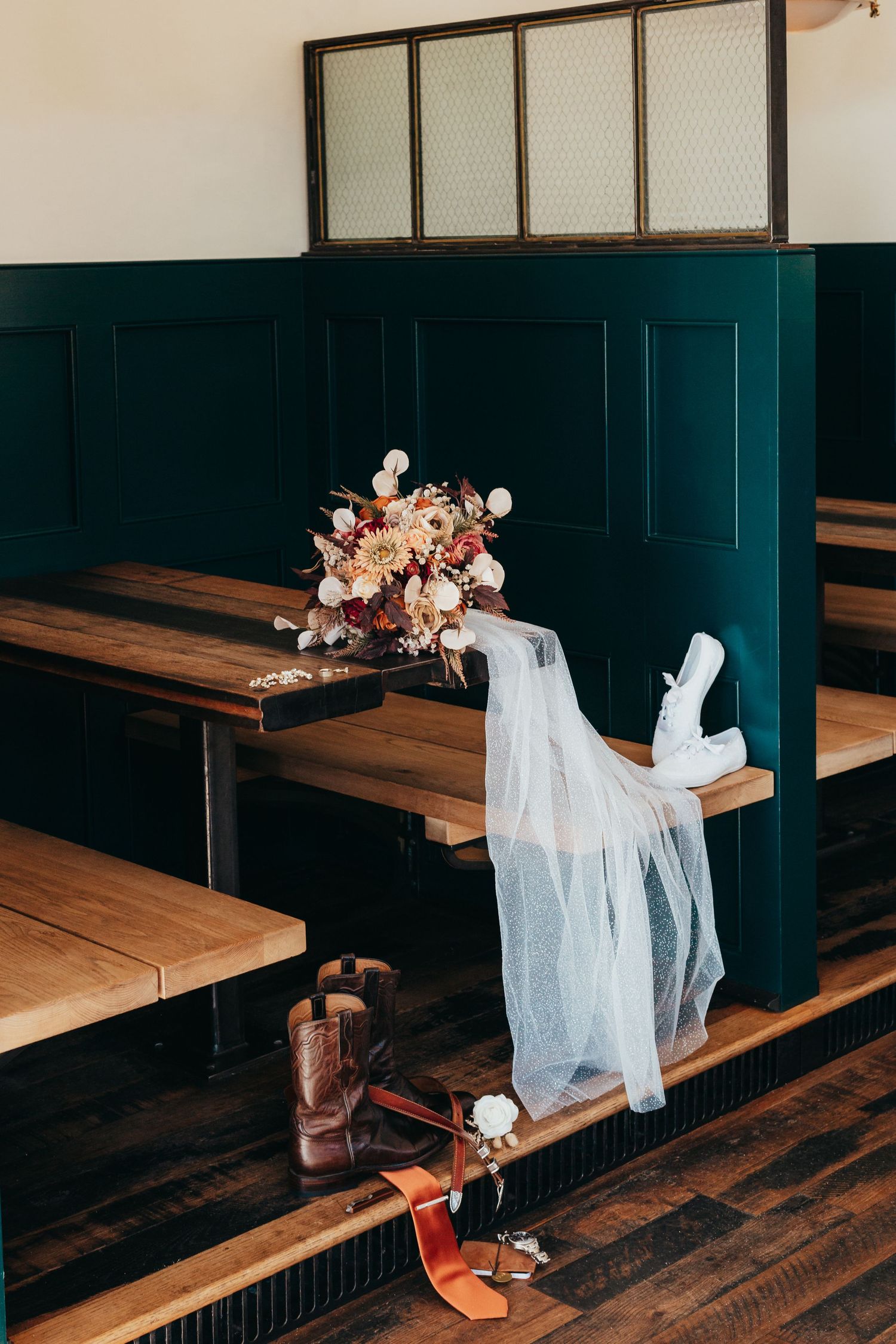 Wedding bouquet and veil artistically arranged on wooden church pews with green paneled walls.