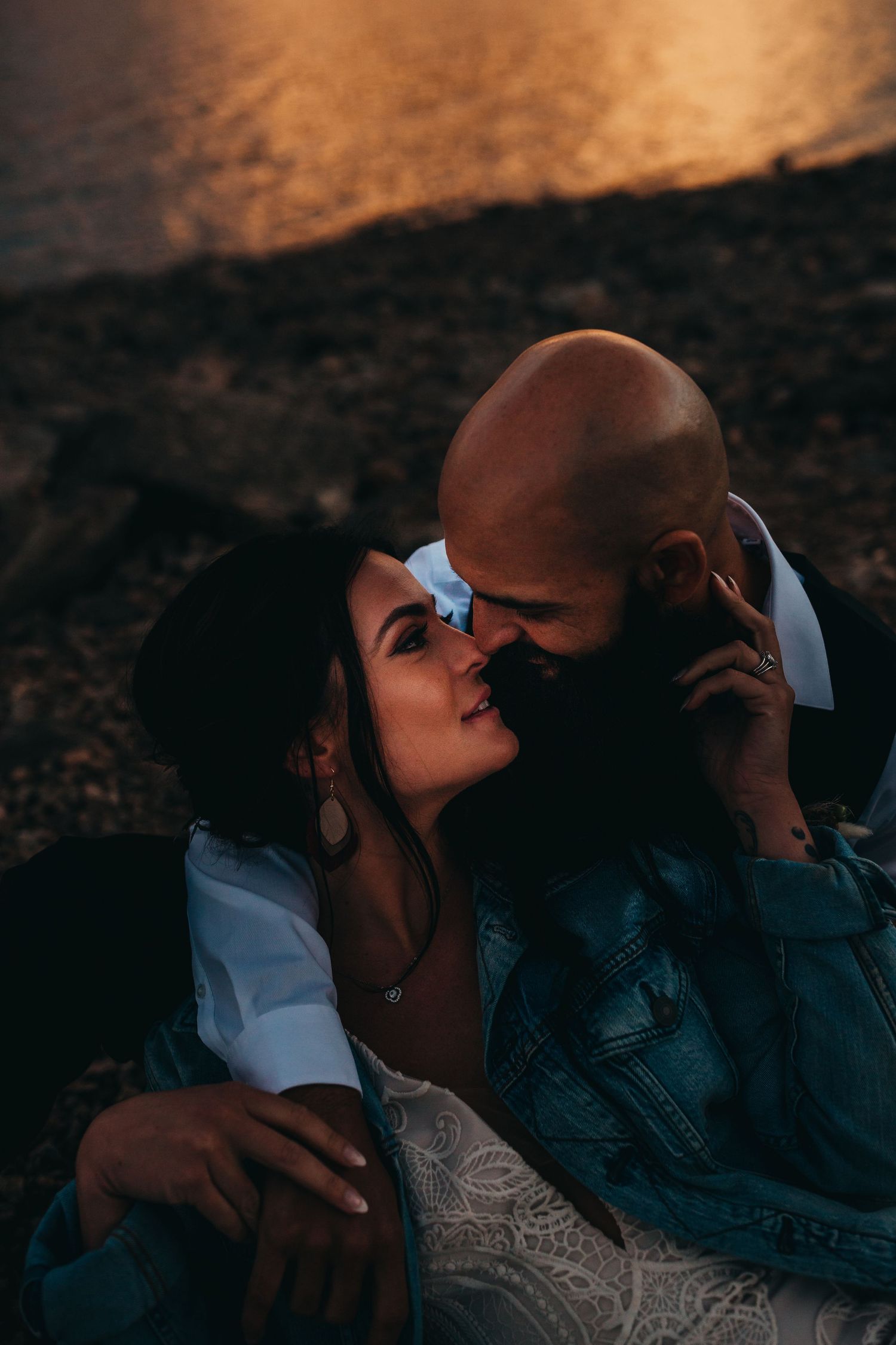 Tender moment between newlyweds during sunset photoshoot by the water.
