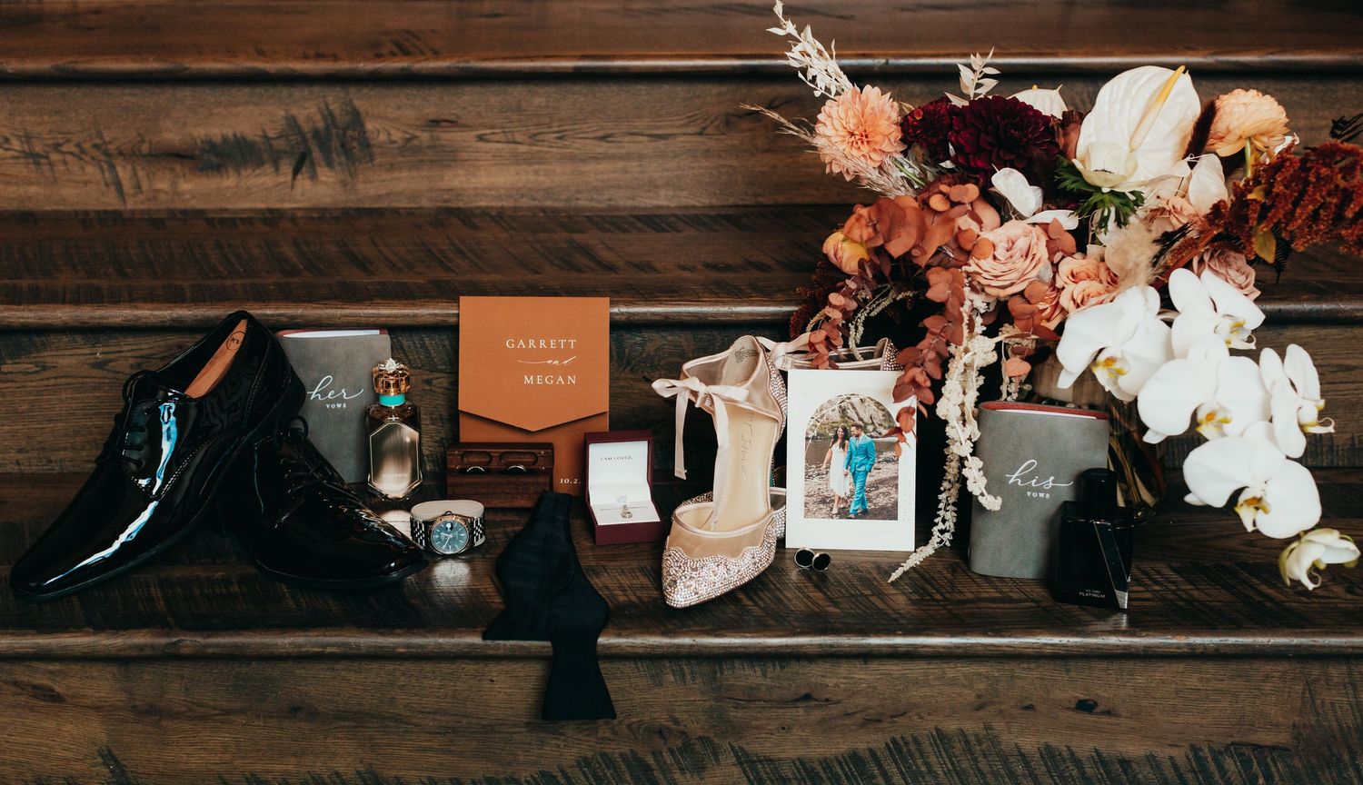 Wedding detail flatlay with dress shoes, flowers and photography on wooden surface.