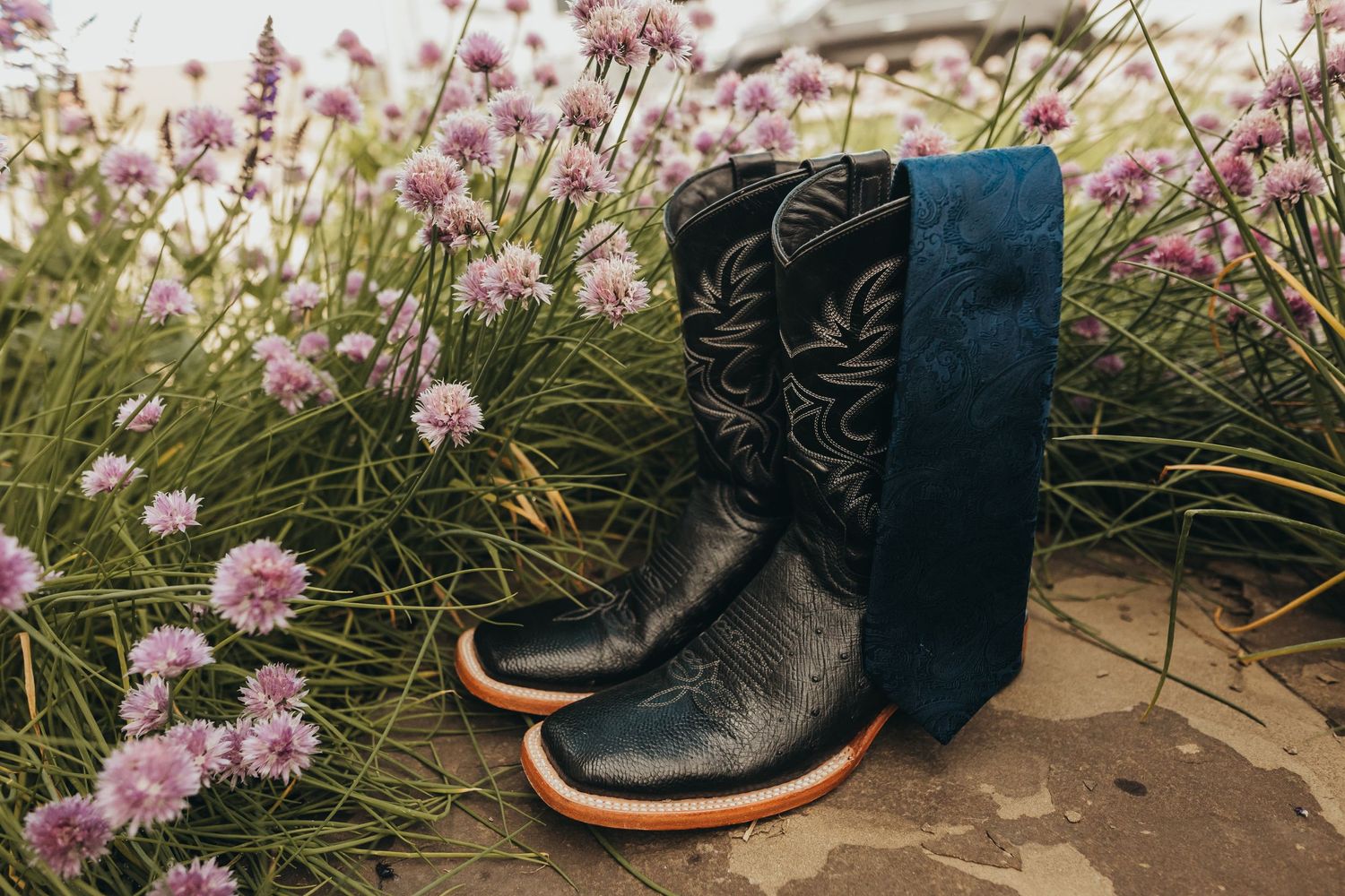 Decorative cowboy boots with floral details displayed among pink wildflowers.