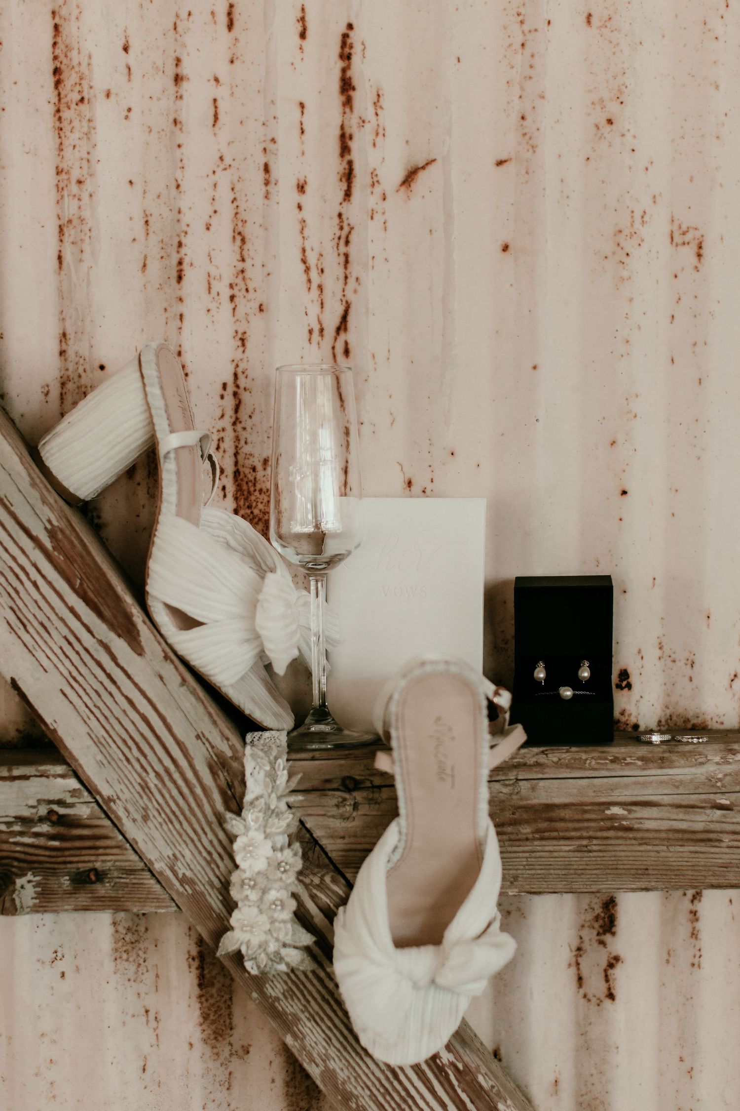Wedding accessories including champagne flutes and white bow heels against rustic wood.