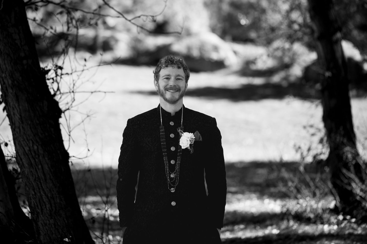 Black and white formal portrait taken outdoors with natural lighting and trees in background.