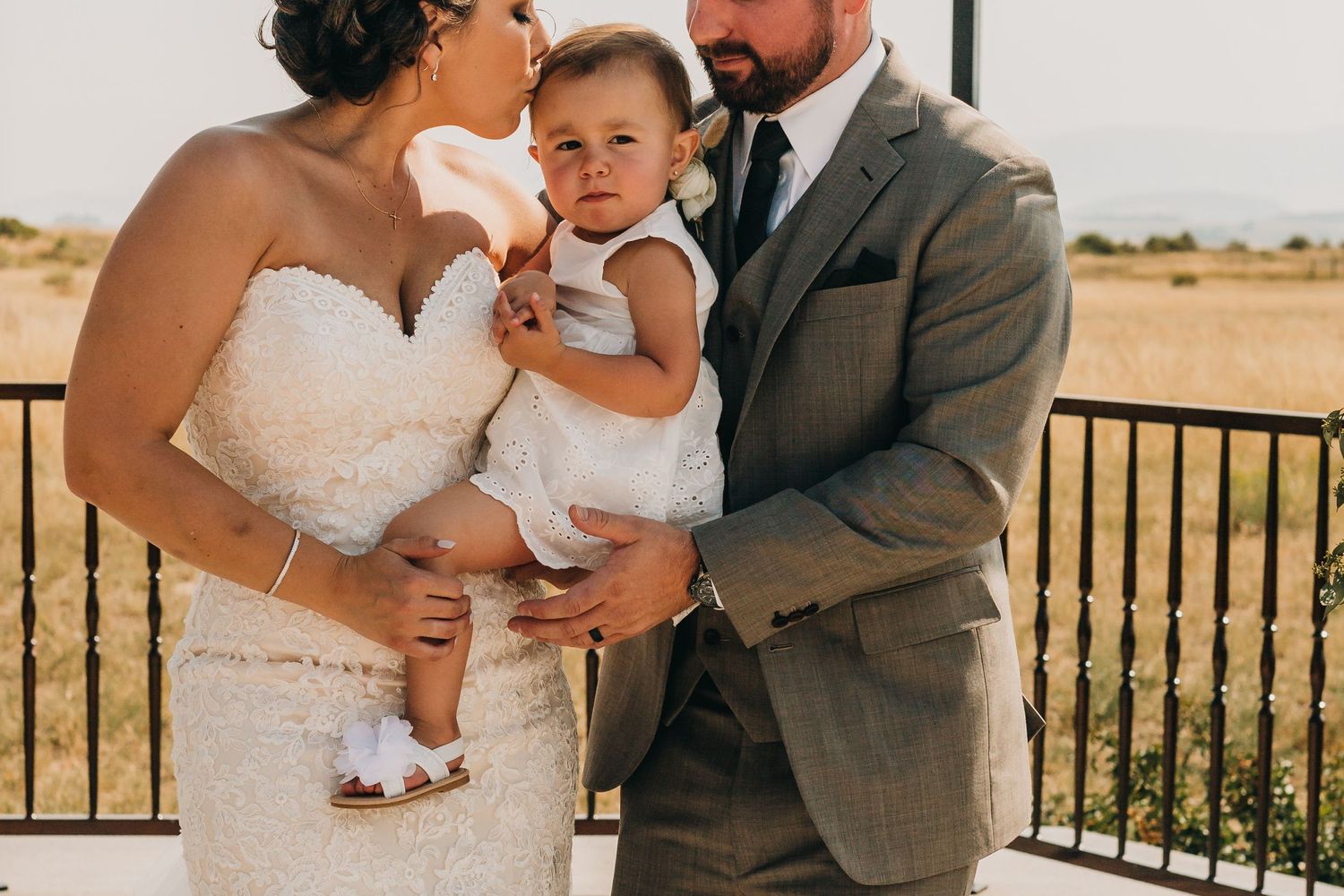 Wedding couple shares tender moment with their baby at outdoor ceremony.