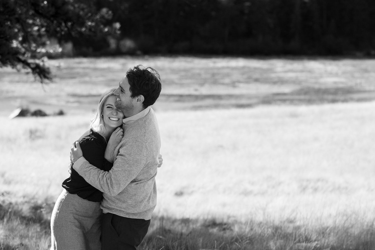 Black and white photo of couple hugging in a sunlit meadow.