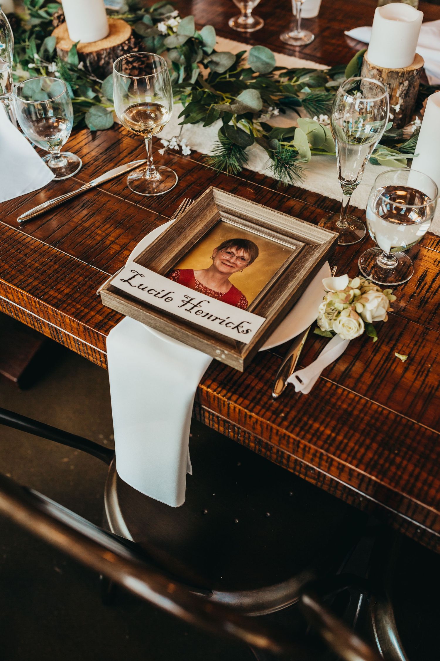 Elegant wedding table setting with framed photo, greenery, and wine glasses.