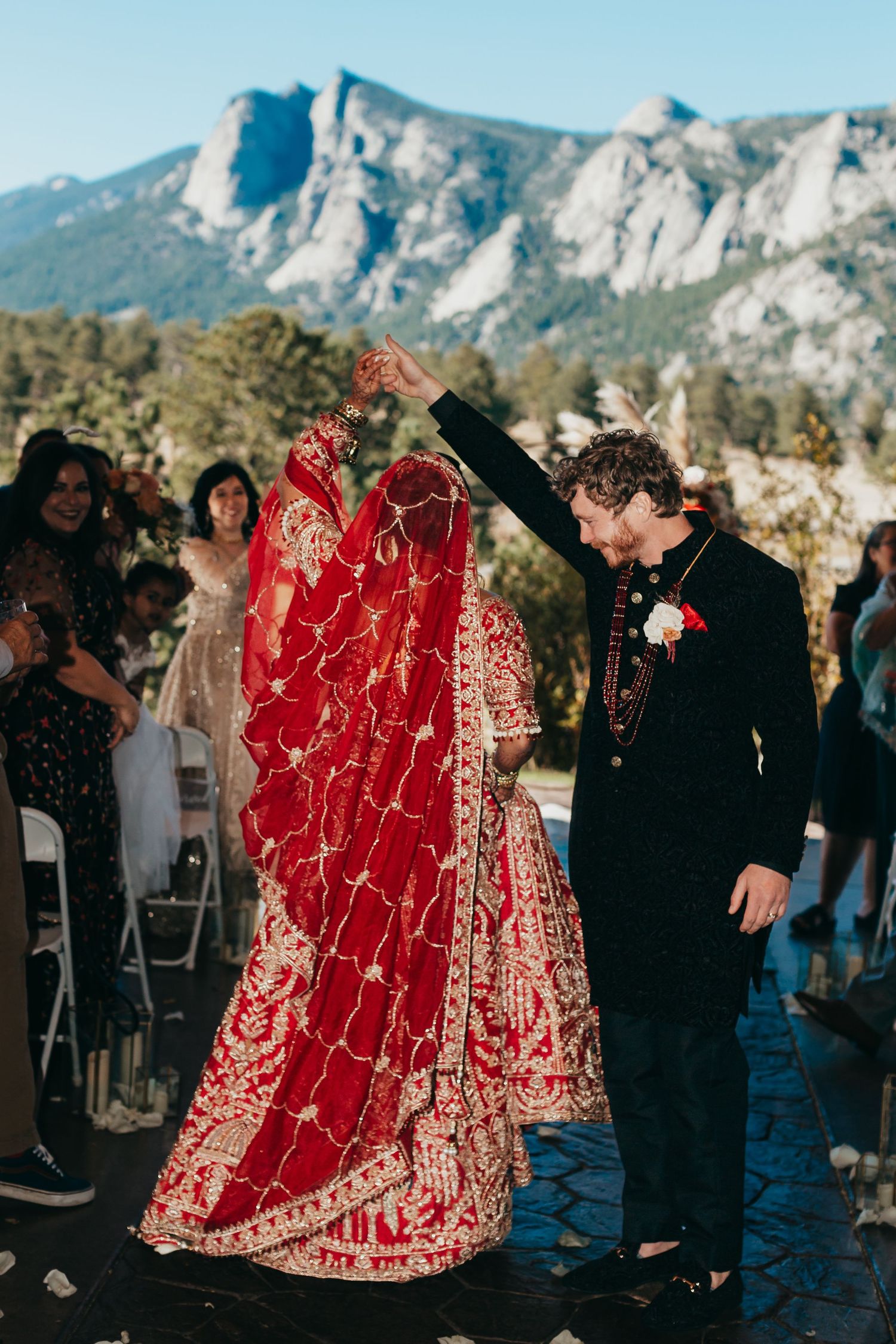 A wedding ceremony set against dramatic mountain cliffs with a traditional red embroidered wedding dress.