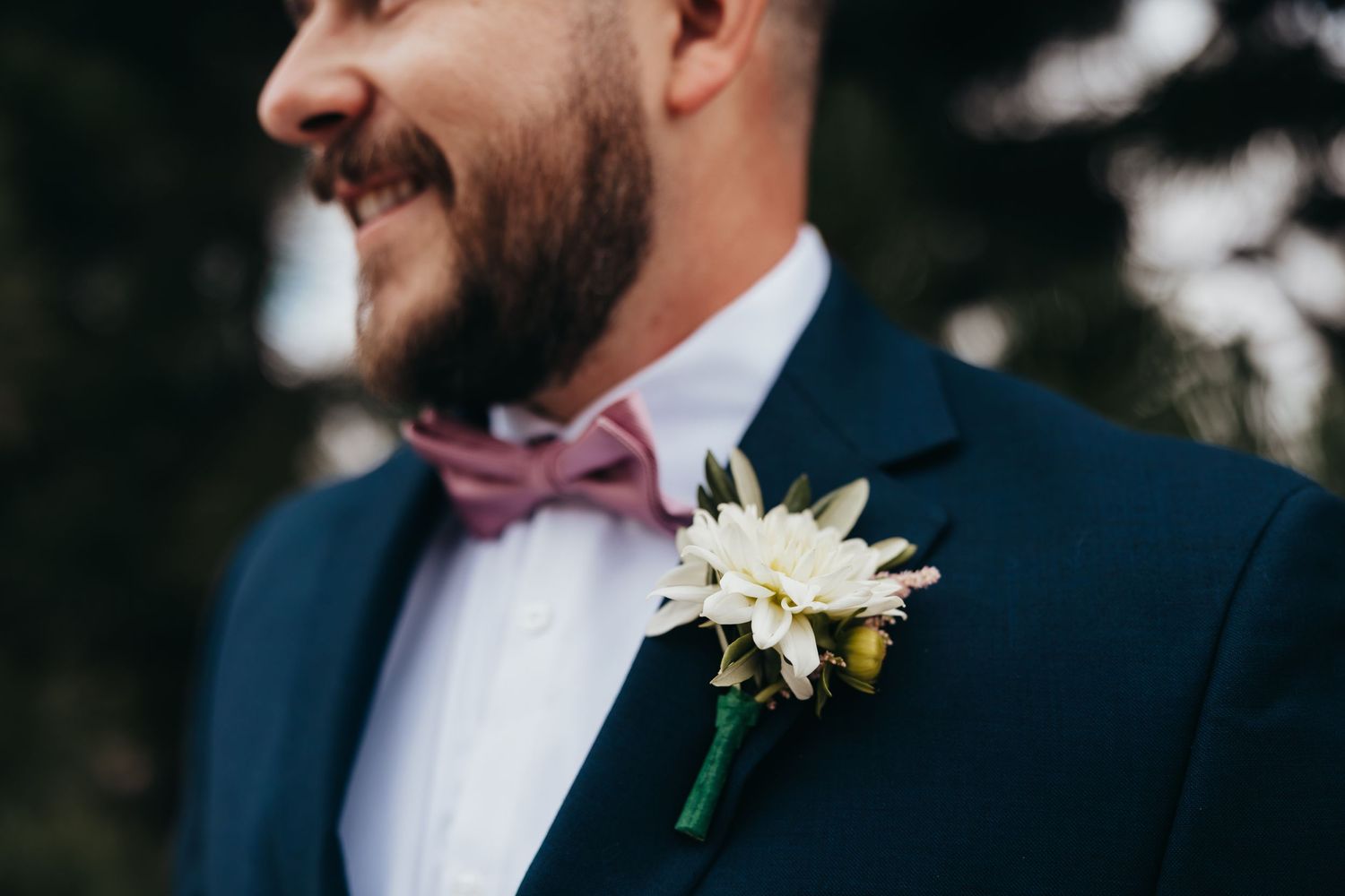 Close-up detail of a navy suit with white floral boutonniere and burgundy bow tie.