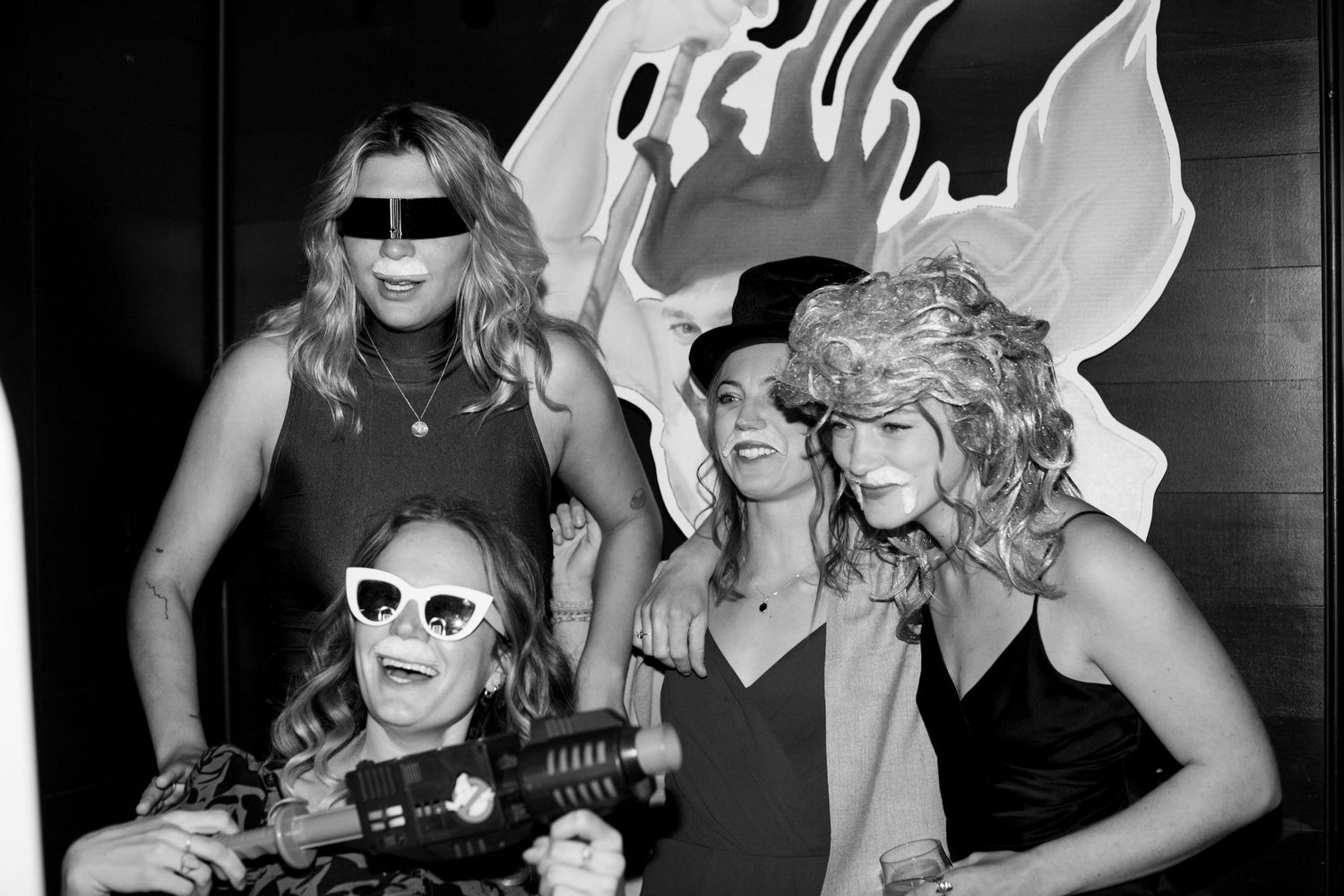 A black and white party photo of friends posing together against an artistic backdrop.