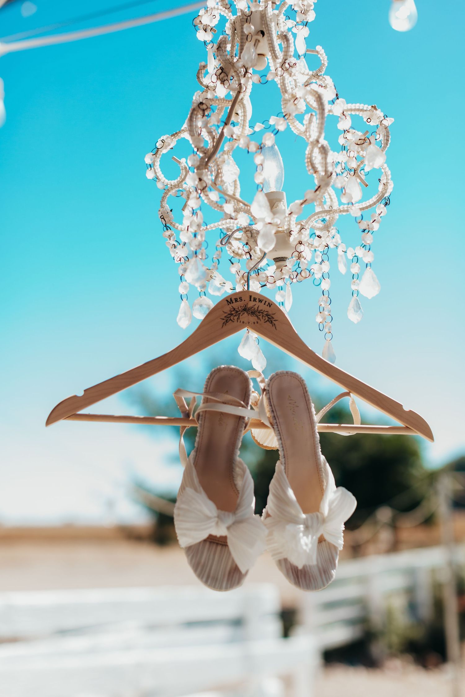 Bridal shoes hanging from crystal chandelier with blue sky background.