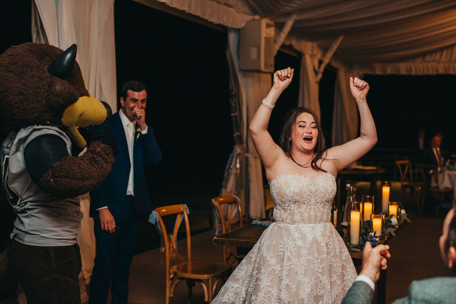An excited bride celebrates with a mascot at a wedding reception.