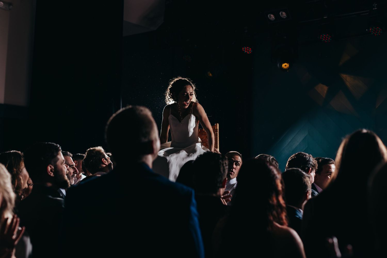 Silhouetted crowd at wedding reception with dramatic lighting.