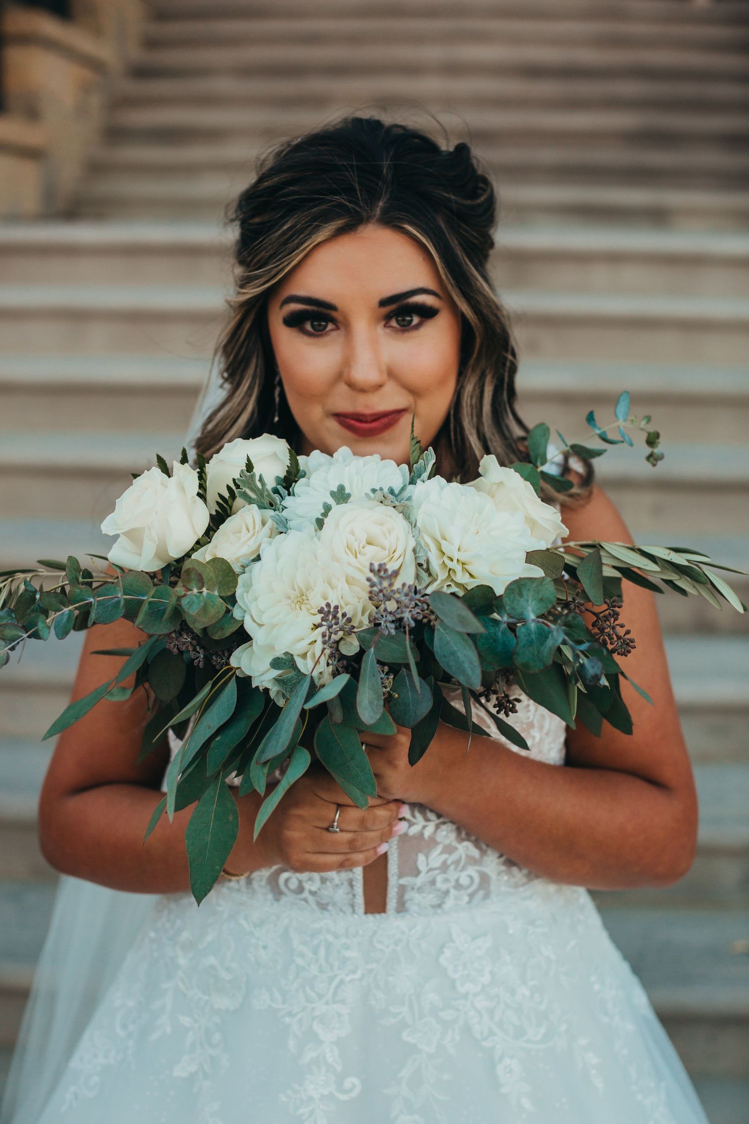 Bride holding elegant white and green bouquet poses on stone steps.