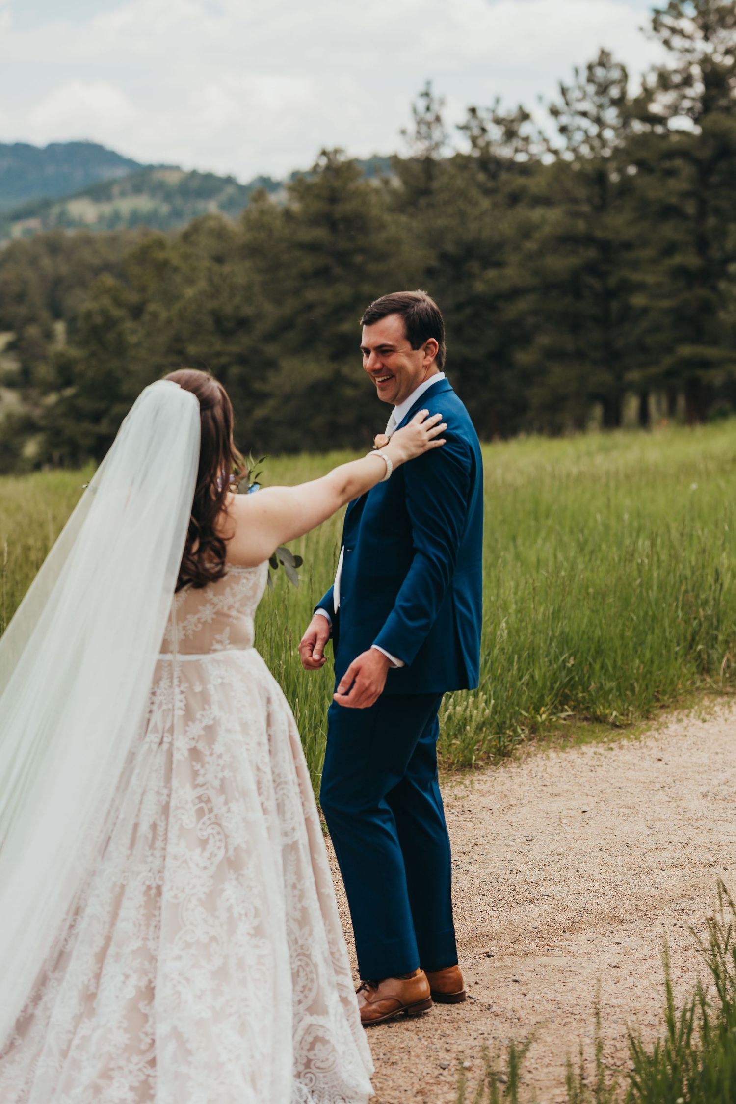 First look moment on a dirt path with mountains and pine trees in the background.