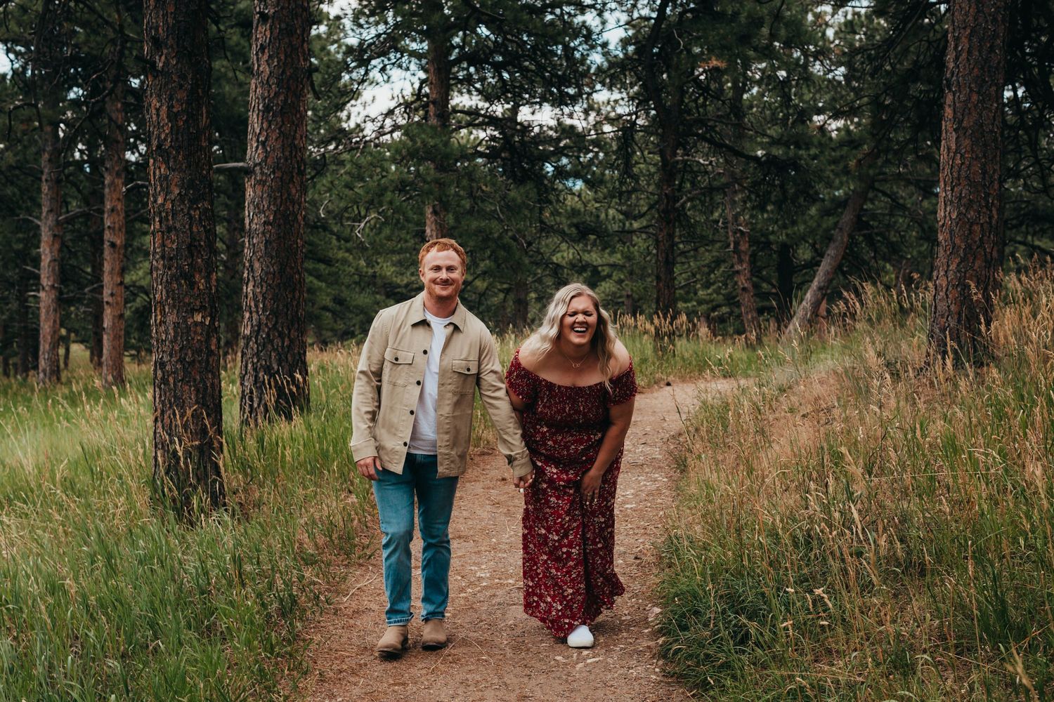 A couple walks together on a forest trail wearing casual attire.