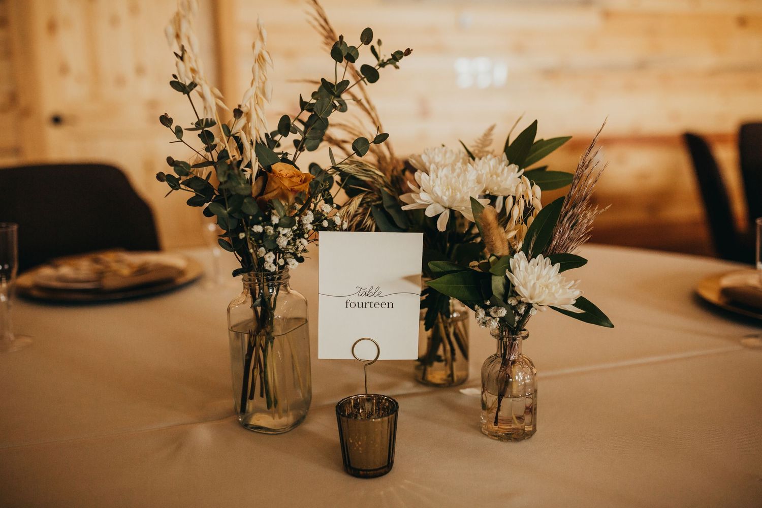 Elegant wedding centerpiece with wildflowers in mason jars and table number card.