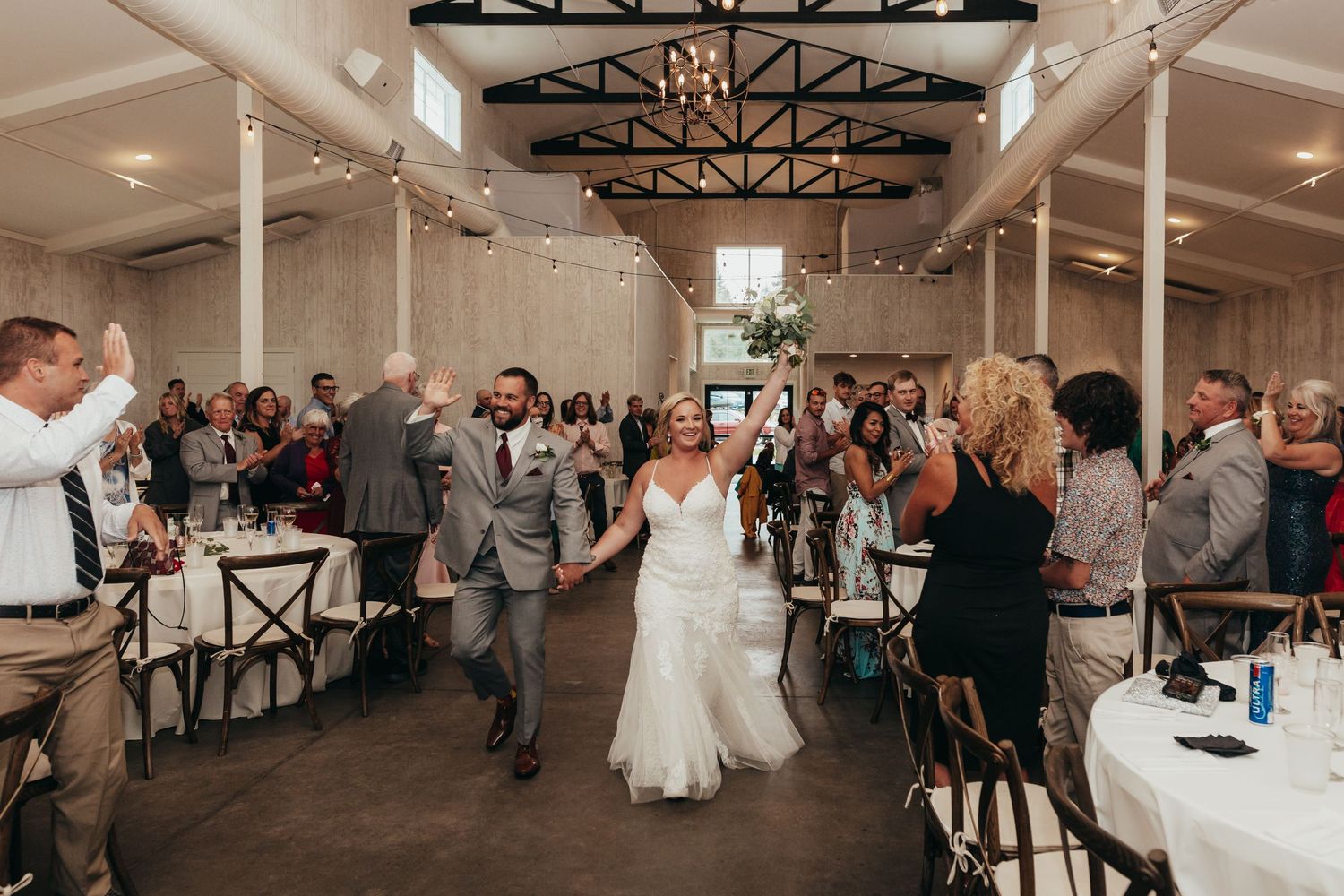 Wedding guests celebrate on the dance floor in an industrial-style venue with exposed beams.
