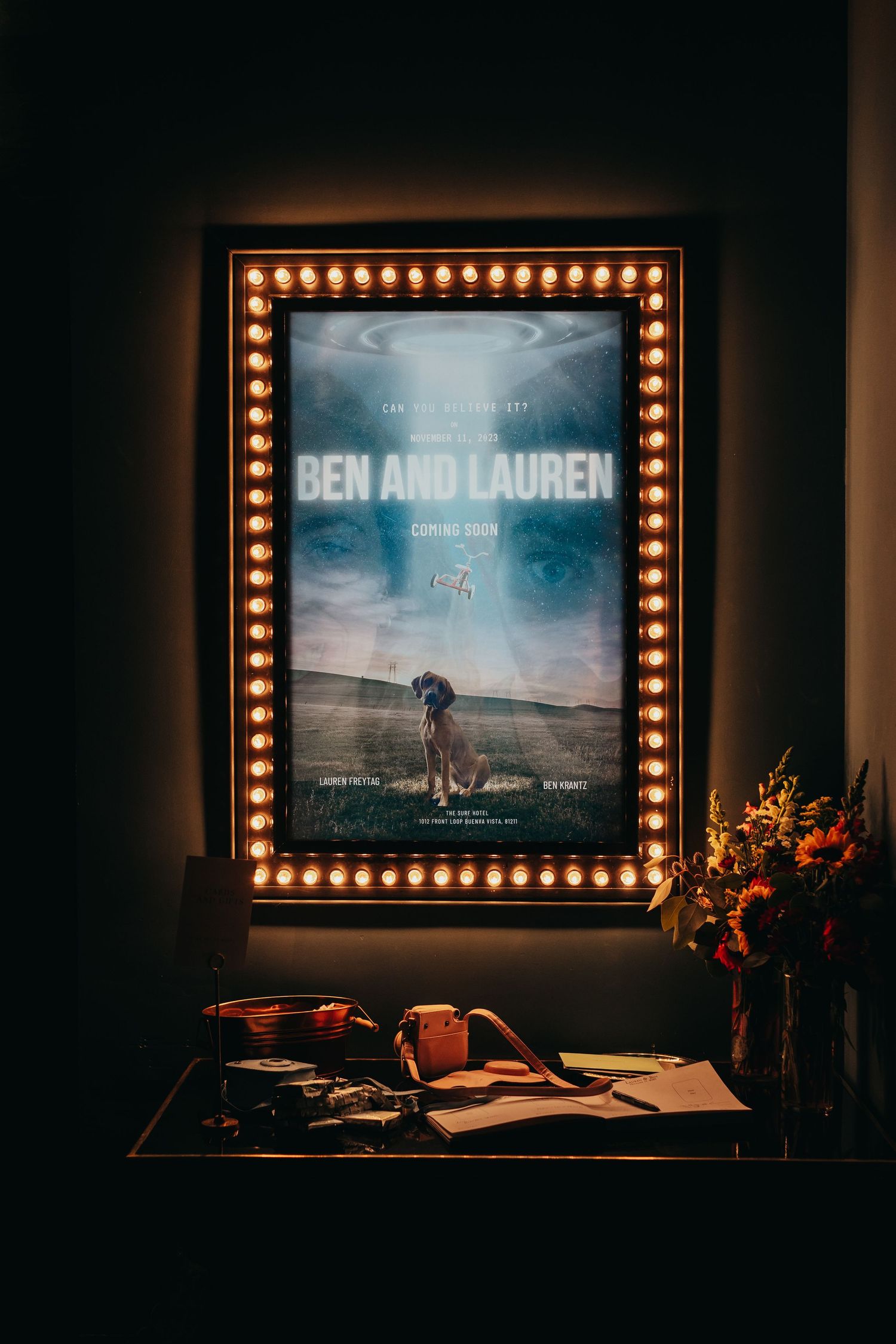 An illuminated movie-style poster display featuring a wedding announcement with marquee lights.