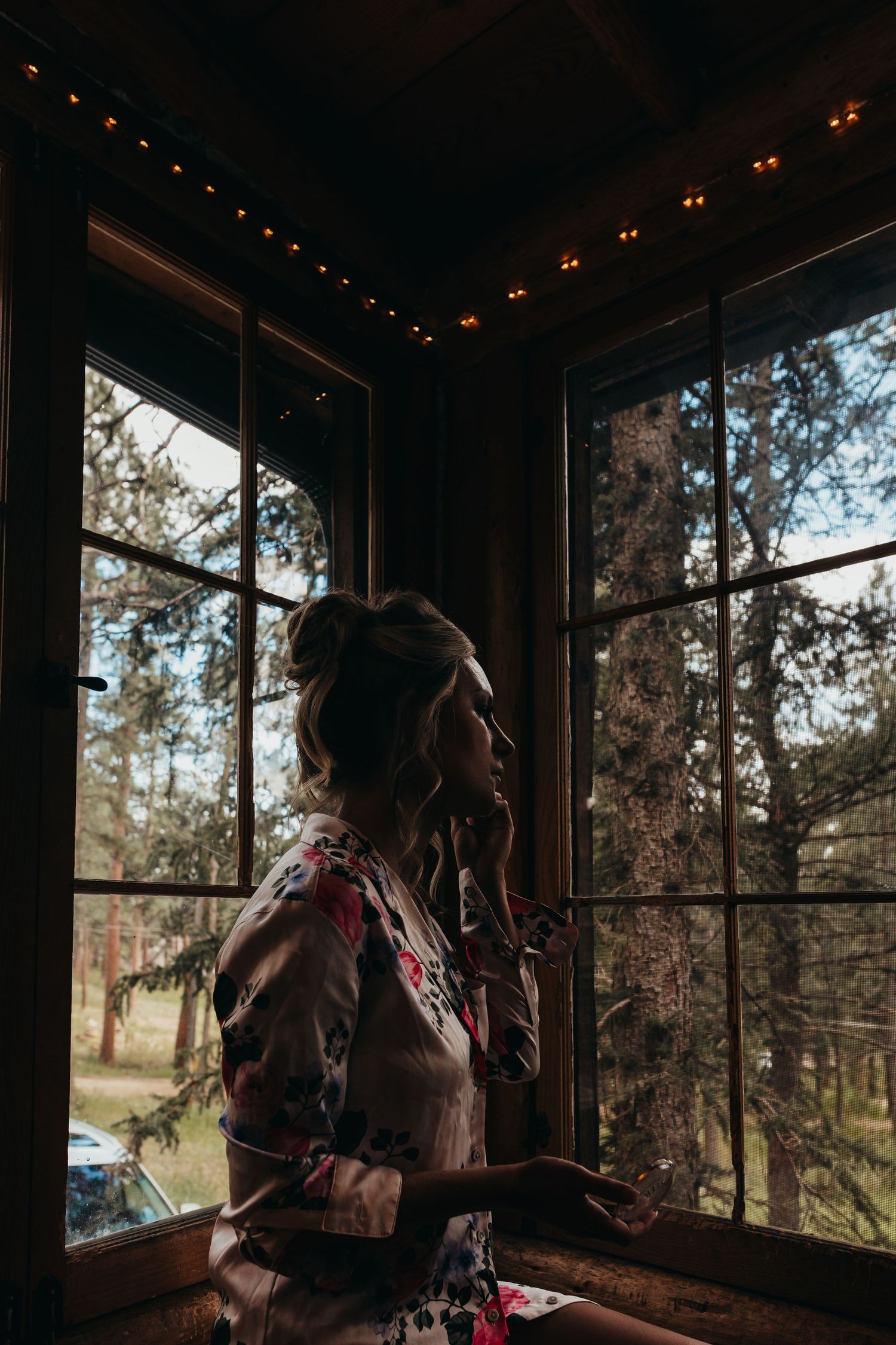 Silhouette of a person in a floral dress looking out a window in moody lighting.