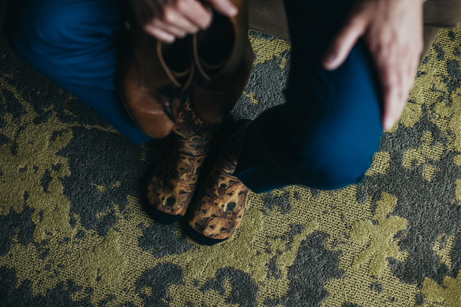 Brown leather dress shoes against an ornate patterned carpet in muted green and gold tones.