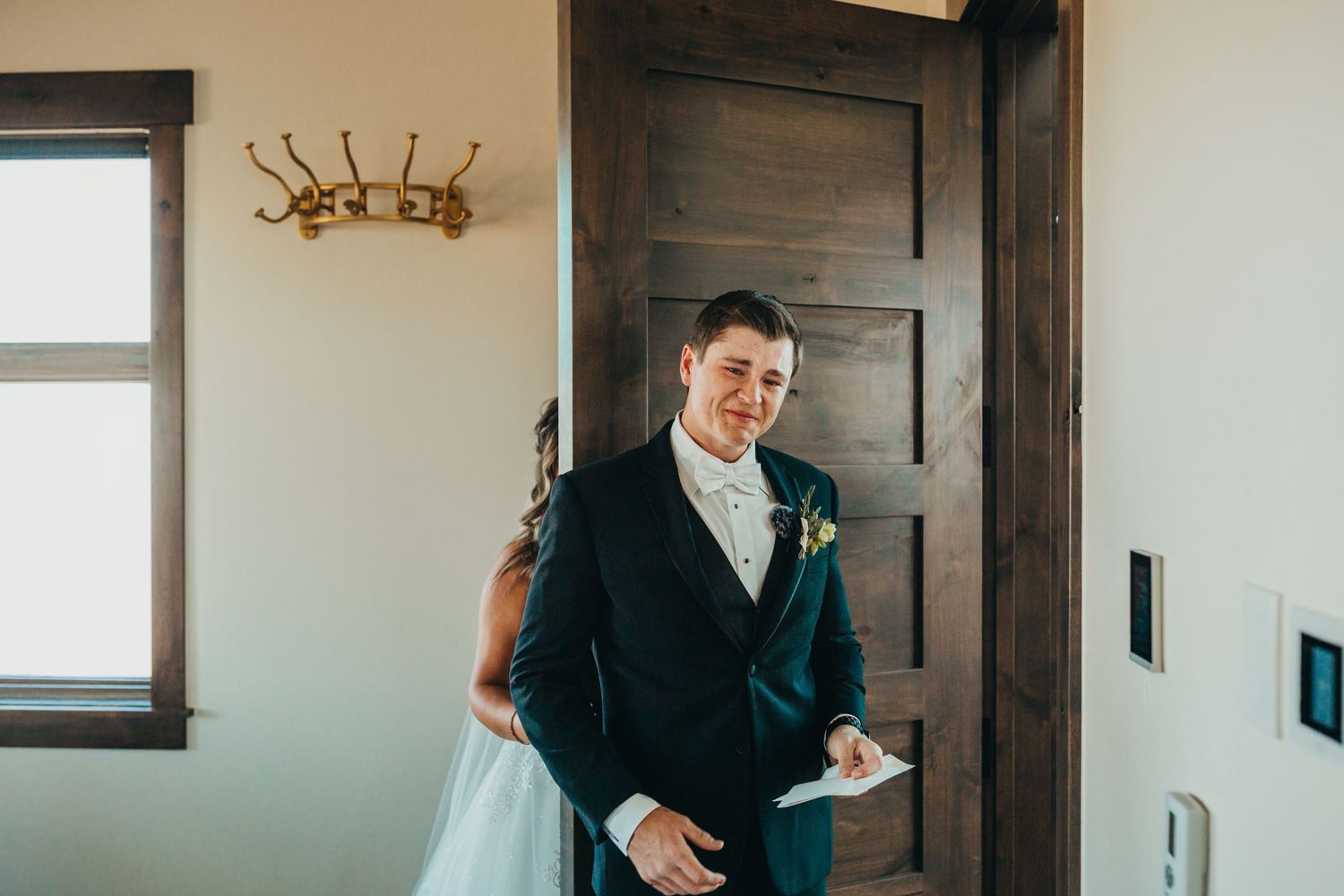 First look wedding moment captured in rustic indoor setting with wooden door.