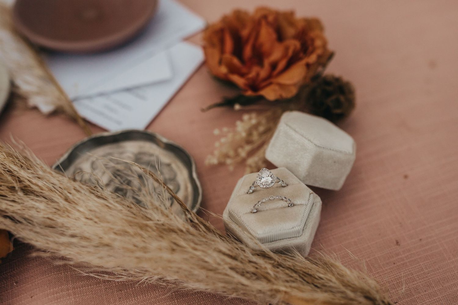 Wedding ring boxes and decor with dried flowers and wheat stalks on a copper surface.