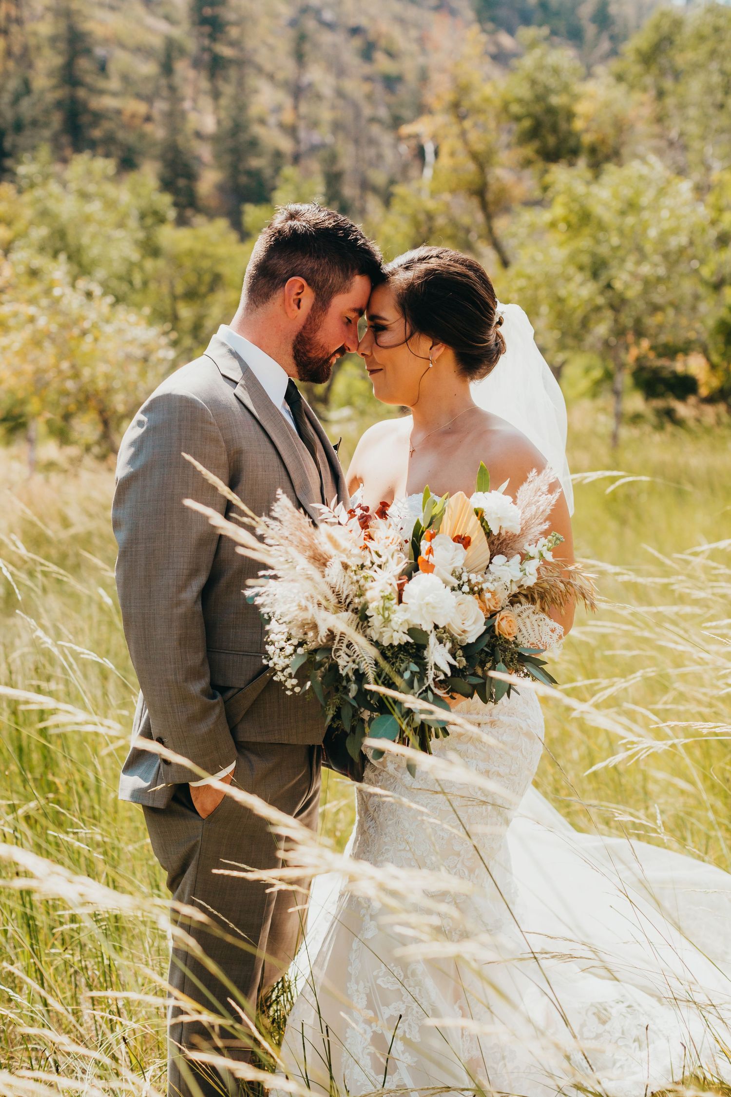 Intimate wedding portrait with couple among tall grasses holding white floral bouquet.