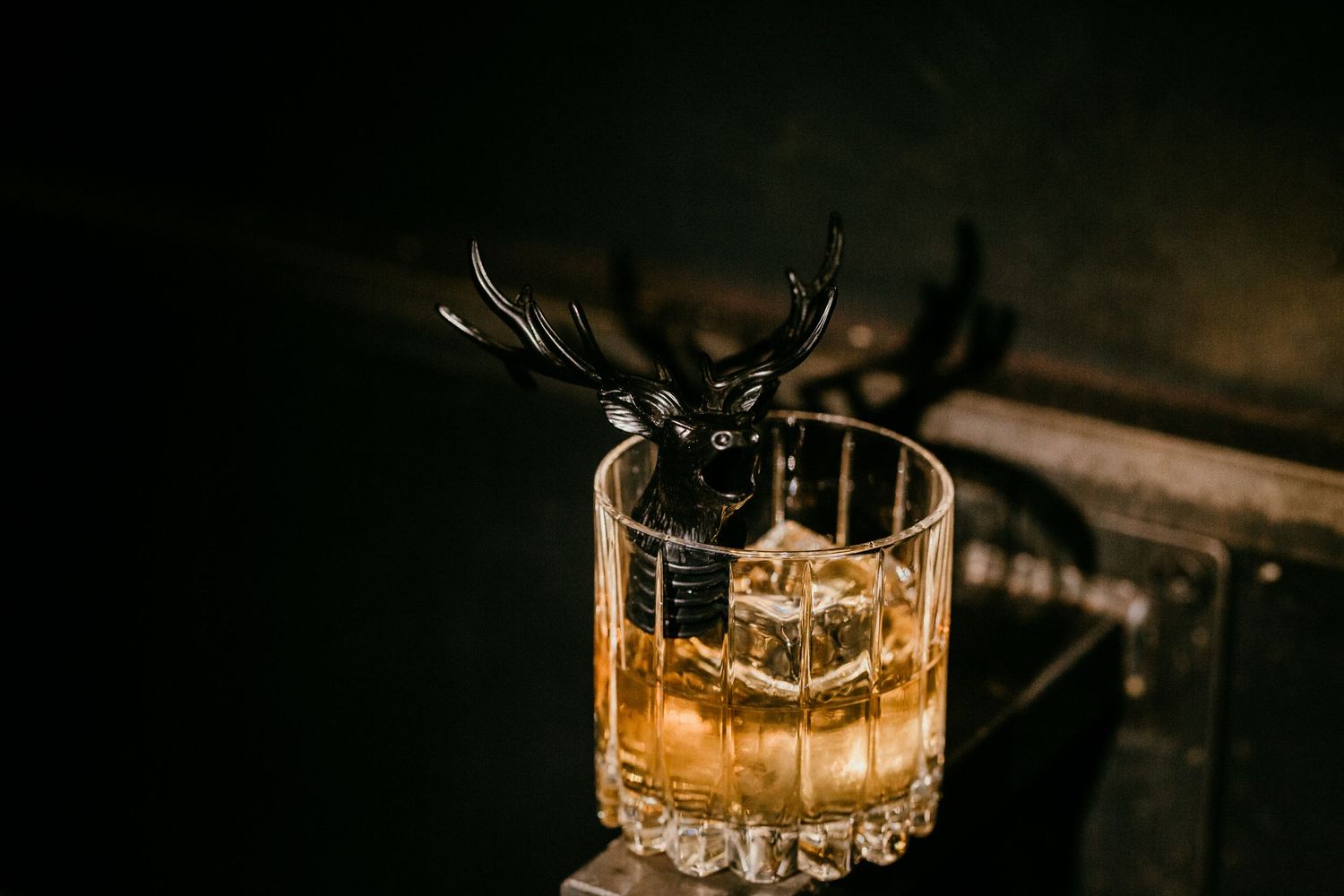 Amber-colored cocktail in crystal glass with dramatic dark background.