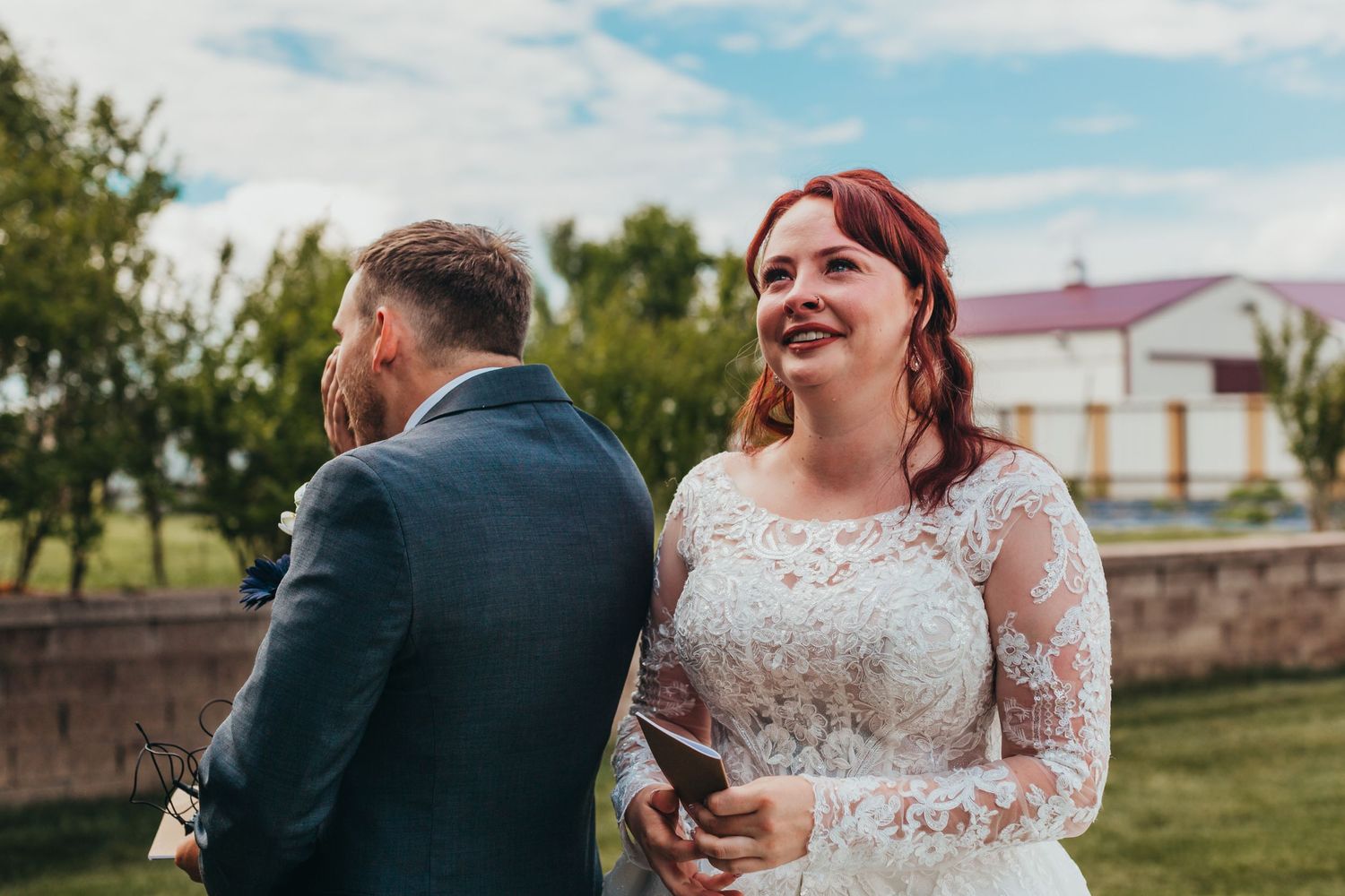A wedding couple shares a candid moment outdoors in front of a rustic backdrop.