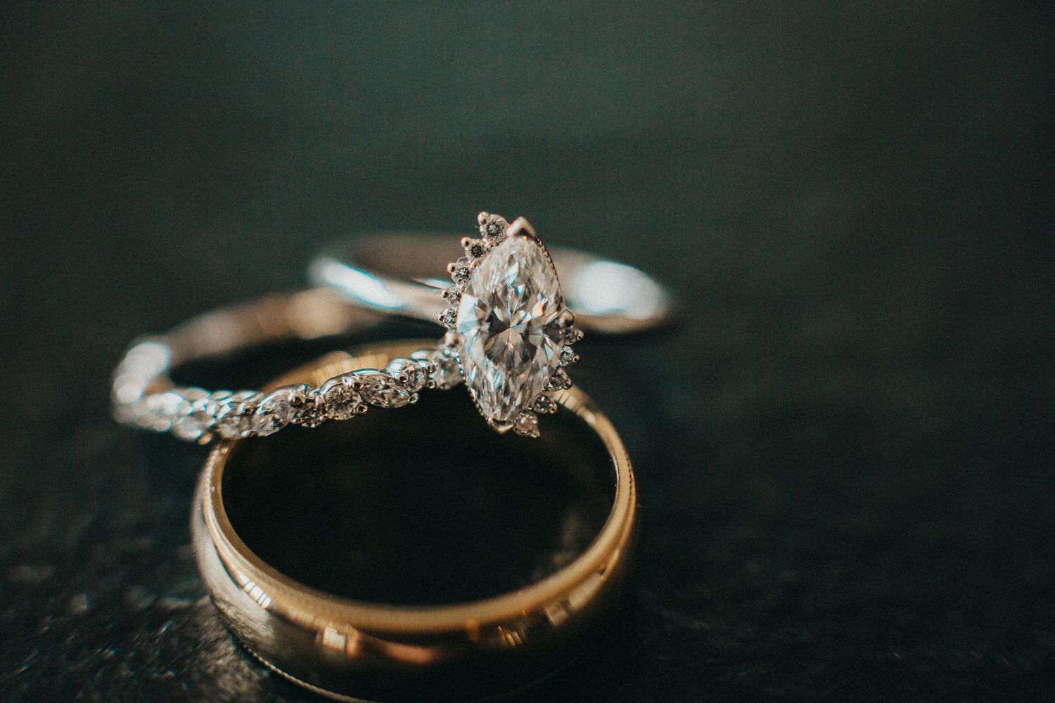 Wedding rings and engagement ring arranged on dark surface with artistic lighting.