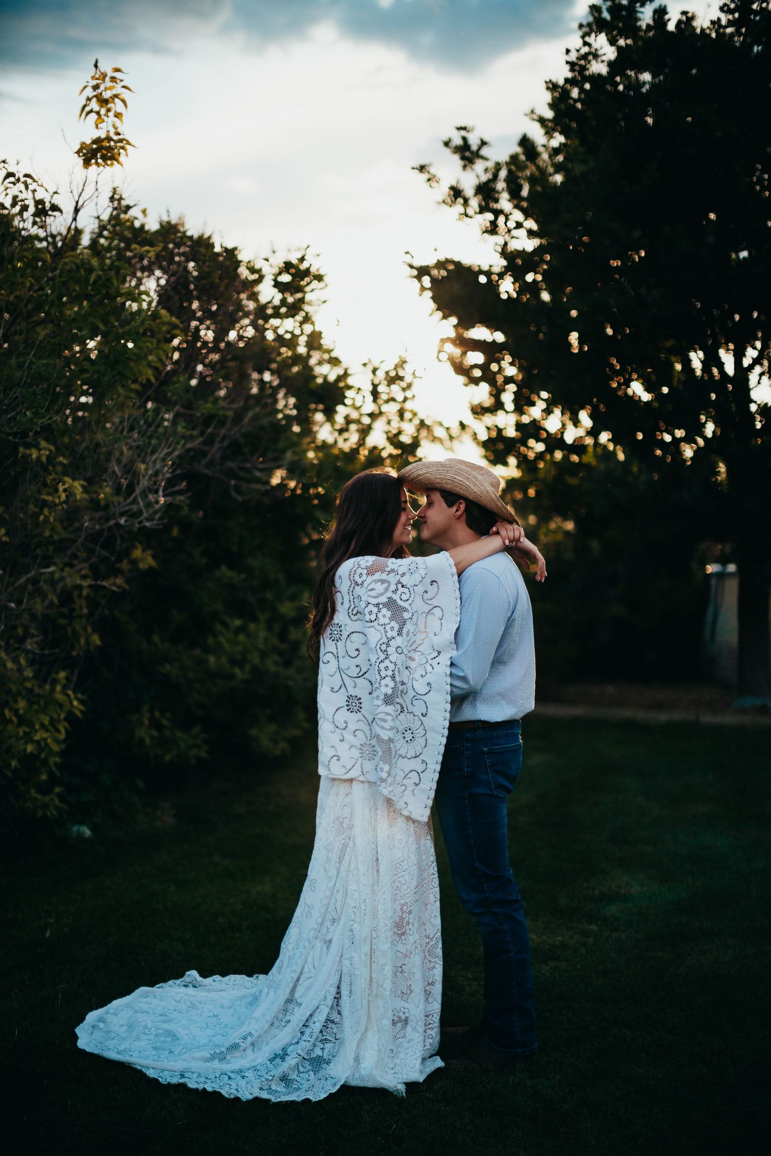 Romantic silhouette of couple in lace wedding dress and cowboy hat at sunset.
