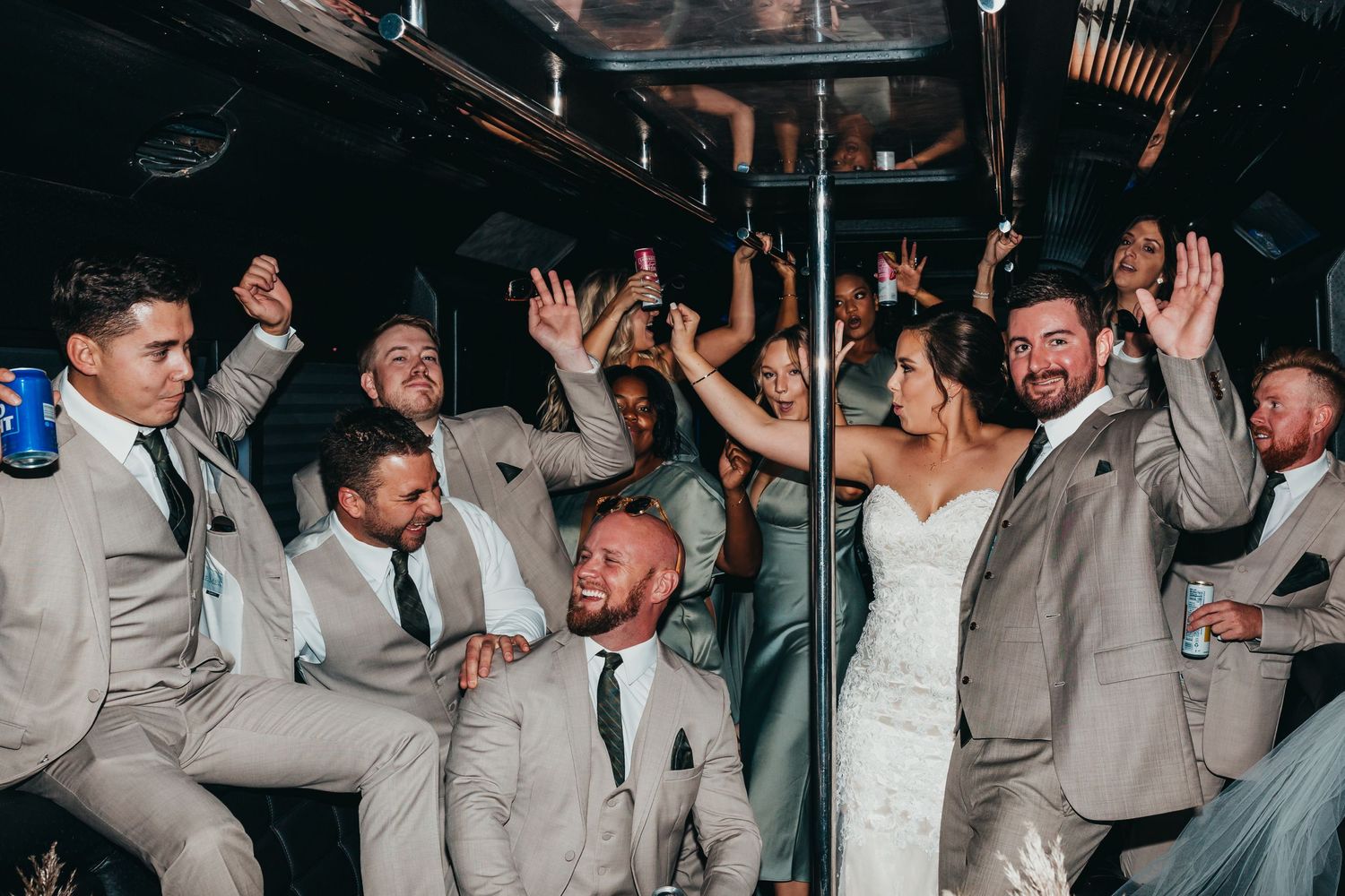Wedding party celebrates energetically inside party bus with raised hands and joyful expressions.