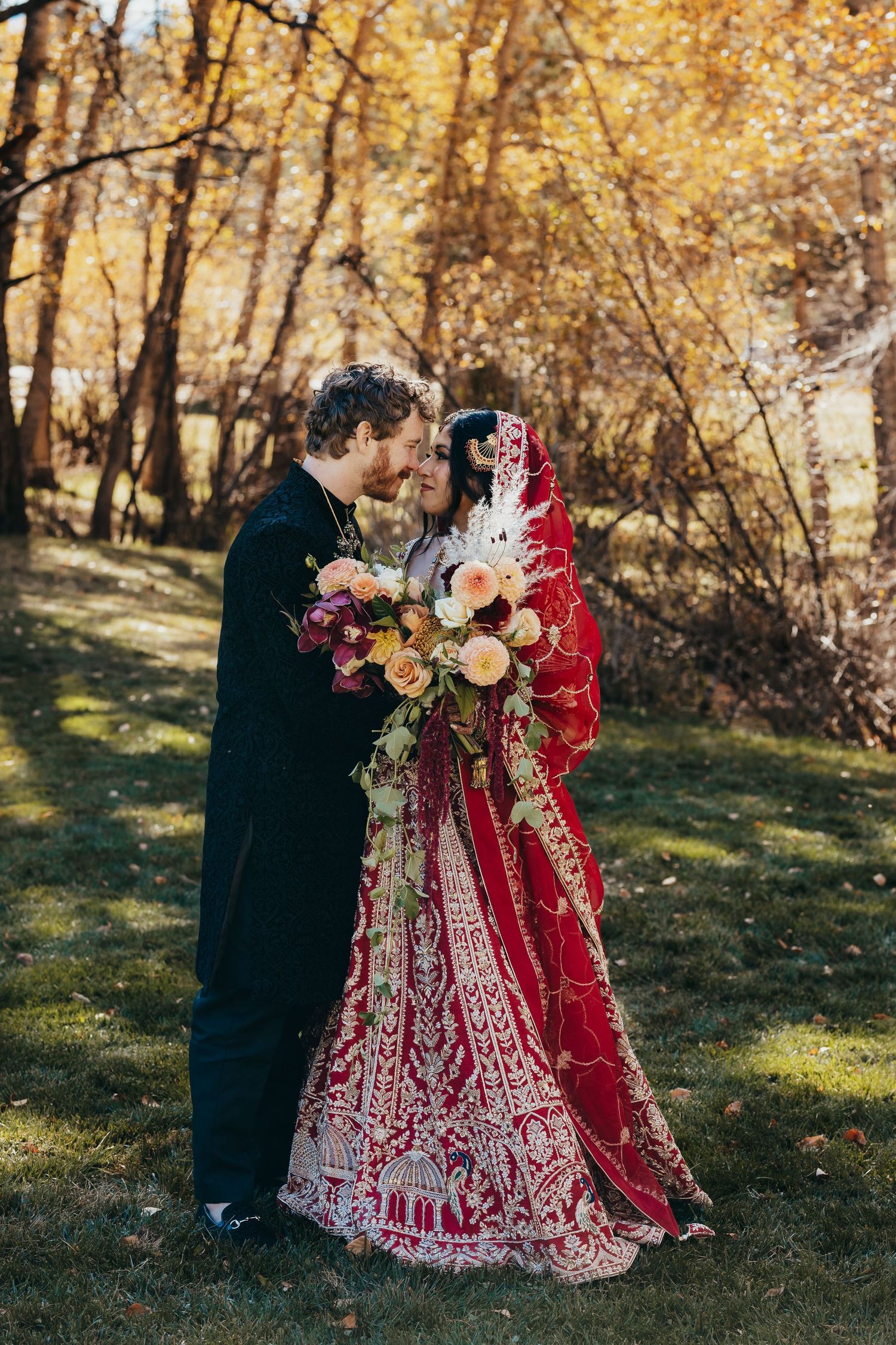 Romantic outdoor wedding portrait with couple embracing against golden autumn trees.