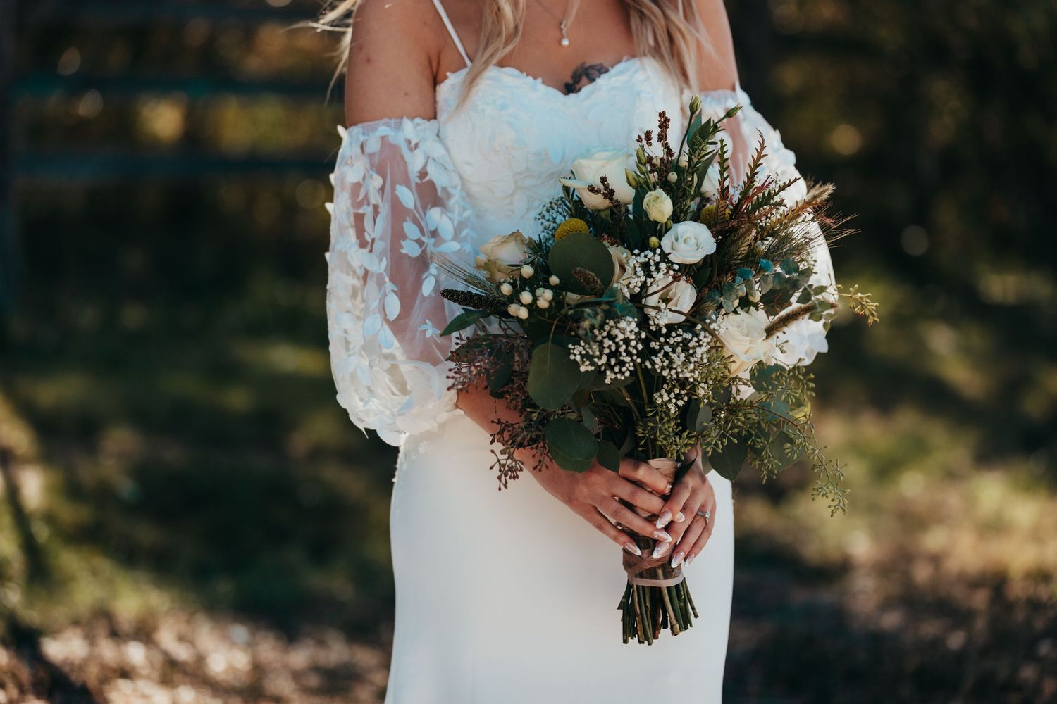 Close-up of white lace wedding gown and natural bouquet with white flowers and greenery.