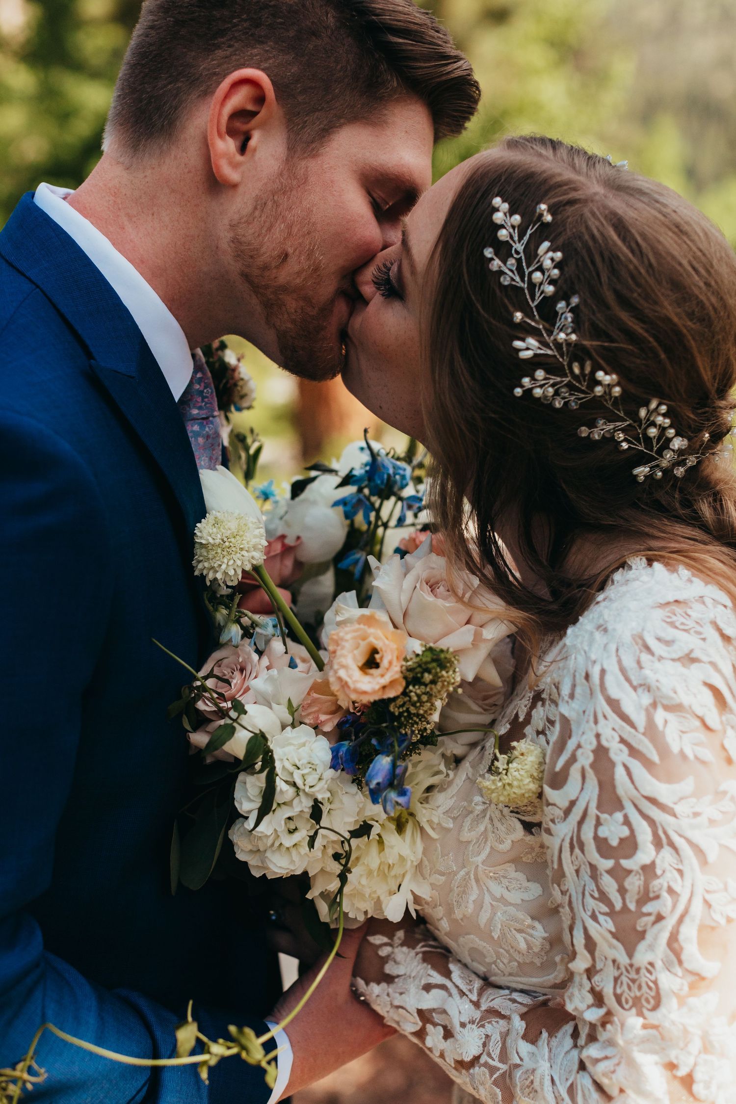 Intimate moment between newlyweds with bridal bouquet against natural backdrop.