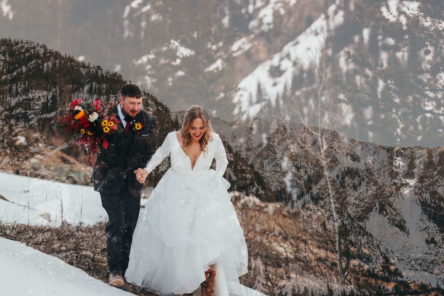 A couple traversing a snowy mountain path during their winter wedding photoshoot.