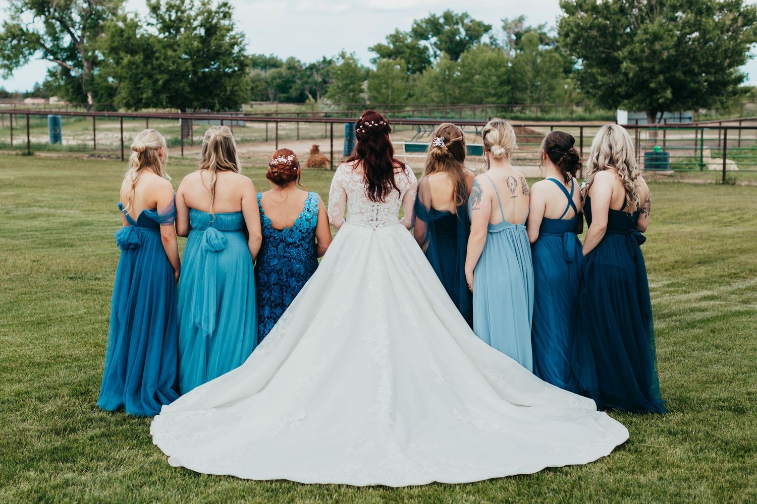 Bridal party shows off blue dresses and train of wedding gown in outdoor garden setting.