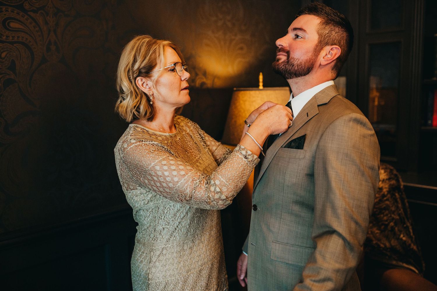 Wedding preparations captured in warm lighting against an ornate wallpaper backdrop.