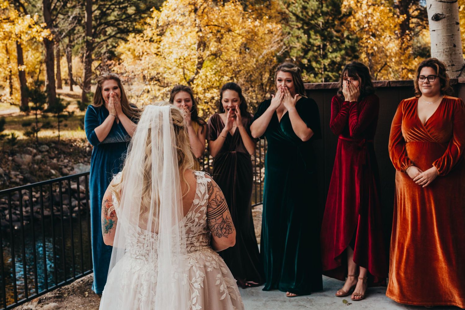 Bridesmaids in colorful dresses react emotionally to seeing the bride in her wedding gown.