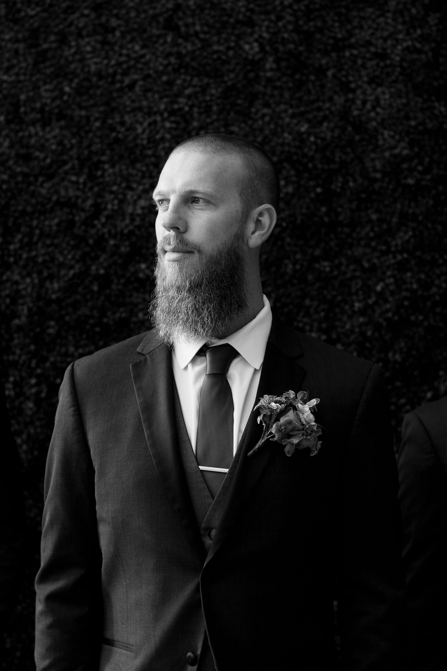 Portrait of a groom in formal black suit with beard against dark textured background.