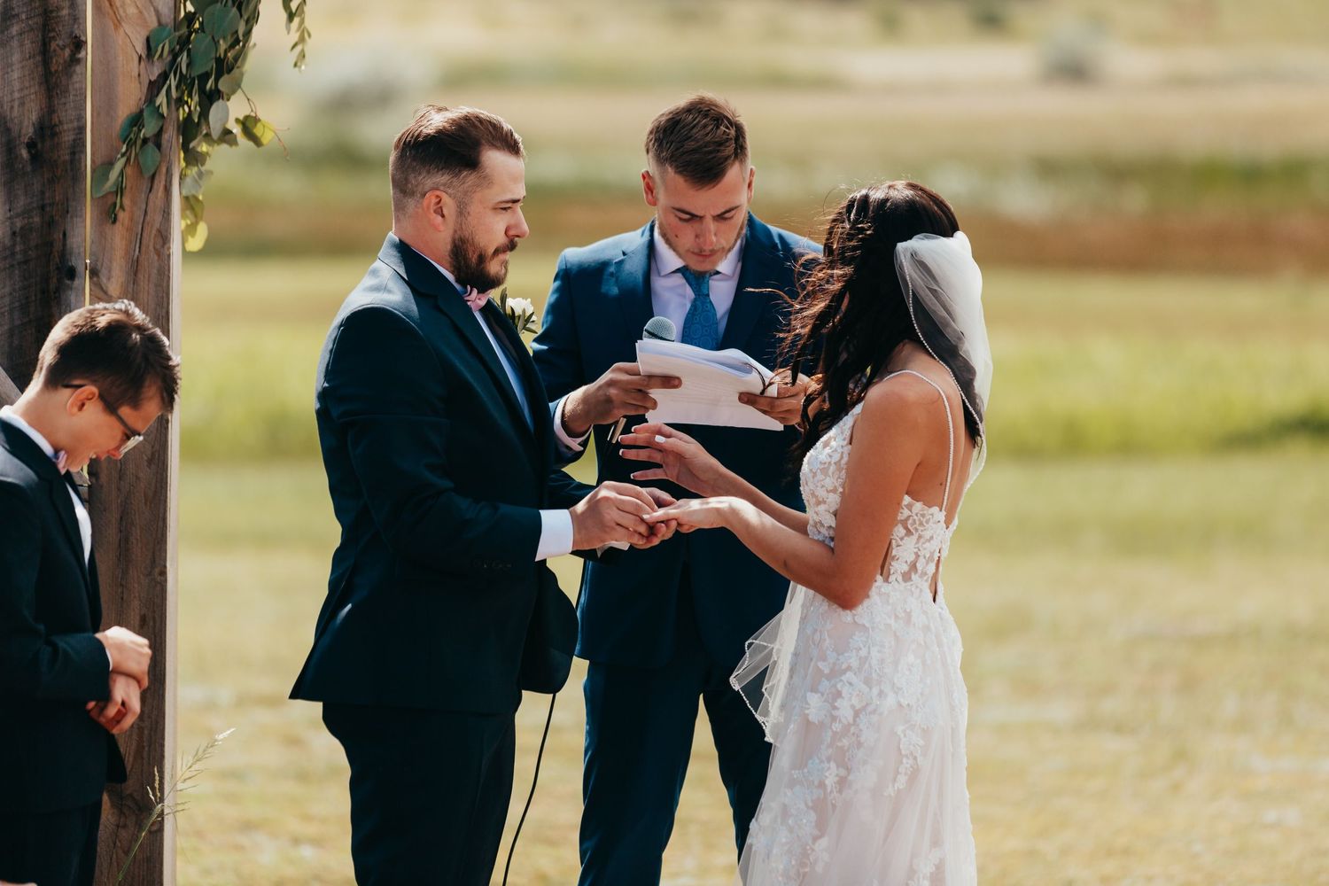 An outdoor wedding ceremony under clear skies with a rustic wooden arch.