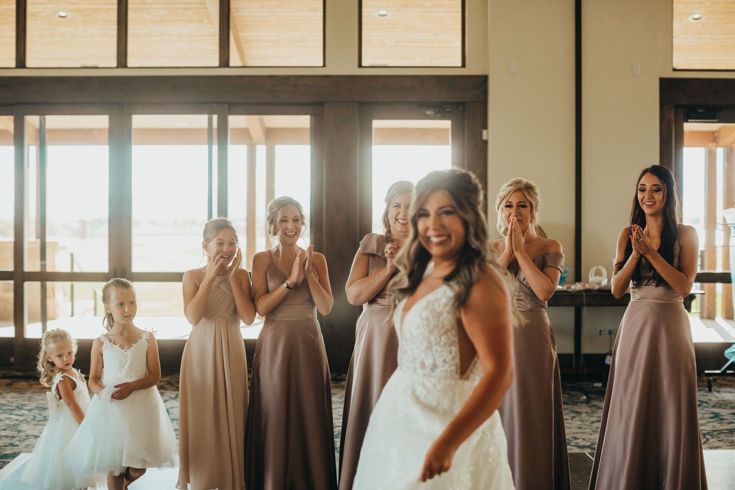 Bride in white lace gown poses with bridesmaids in mauve dresses during wedding preparations.