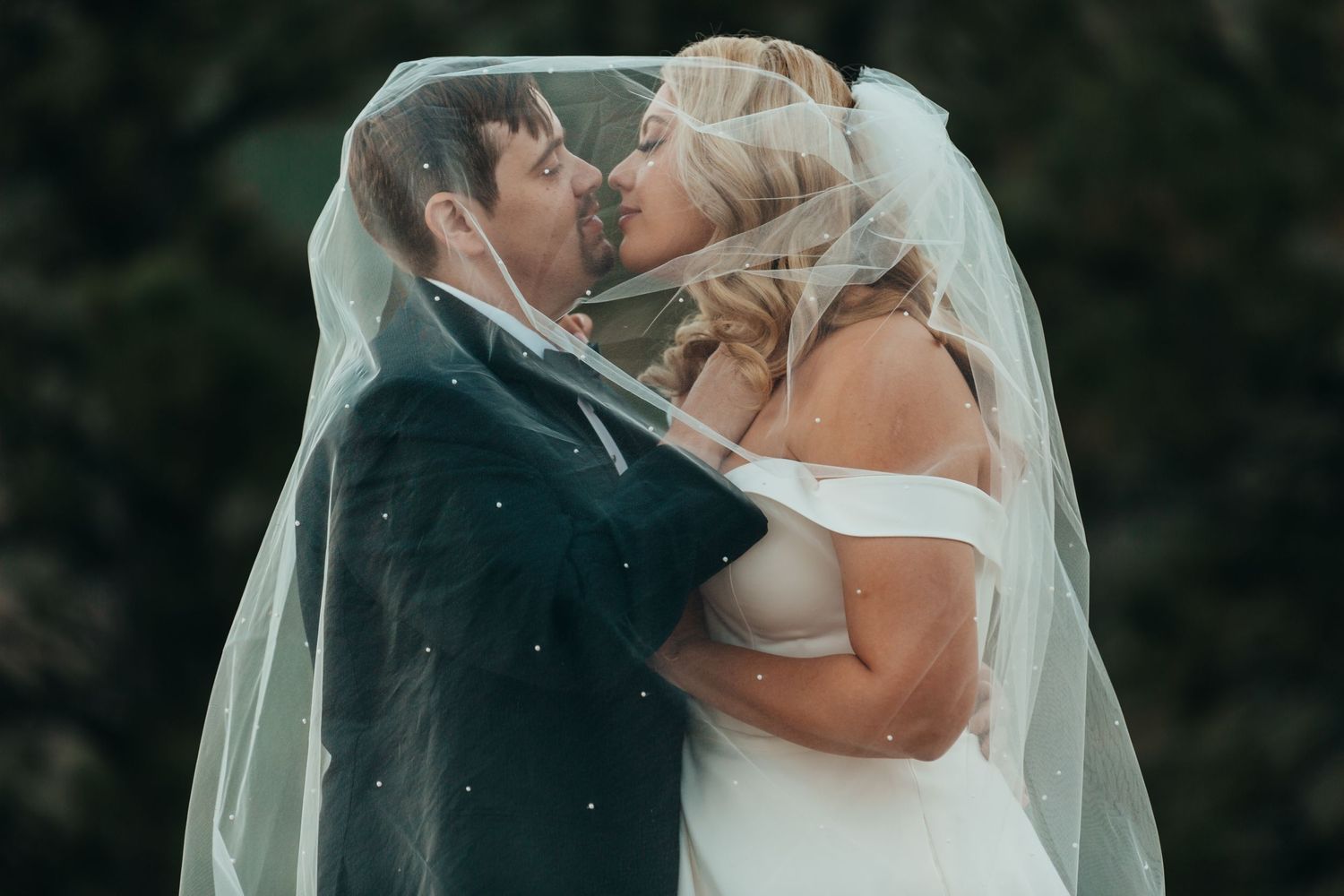 A romantic wedding kiss moment captured outdoors with the bride in white and long flowing veil.