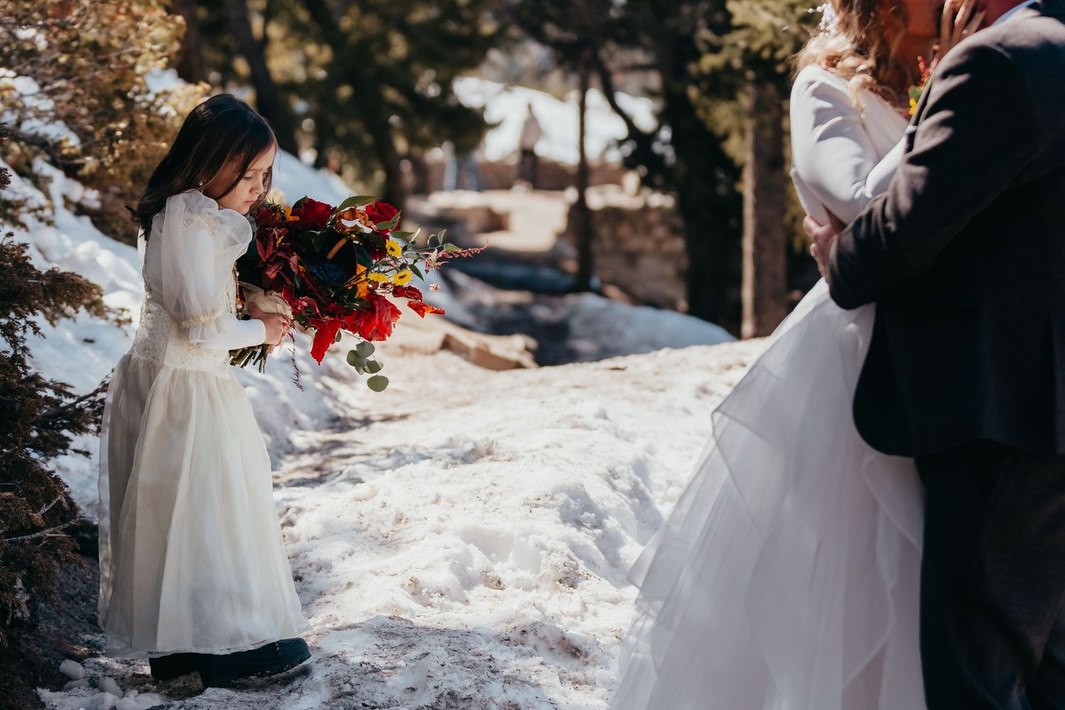 Wedding party members in white dresses hold vibrant red bouquets in the snow.